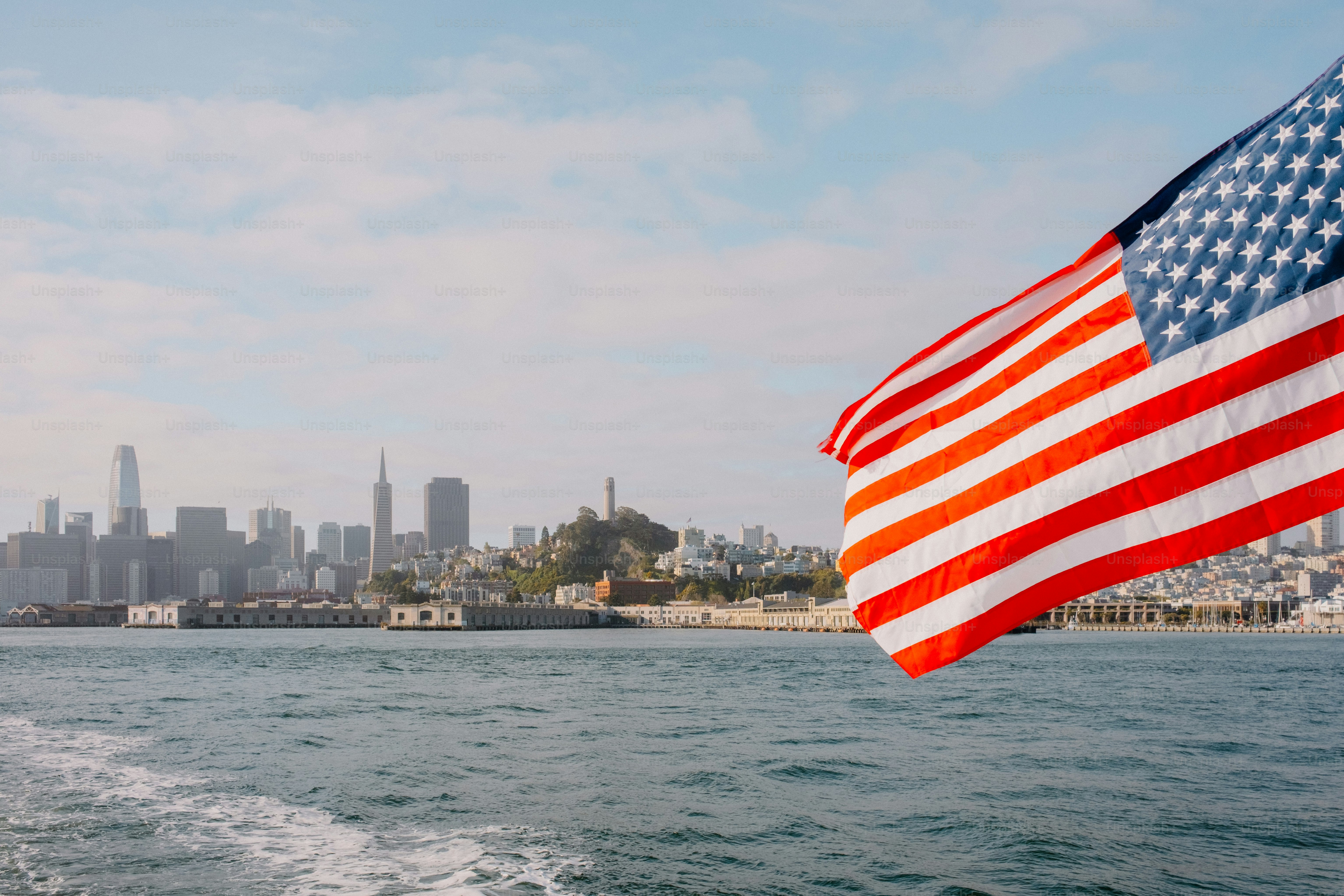 The american flag waves over a city and water.