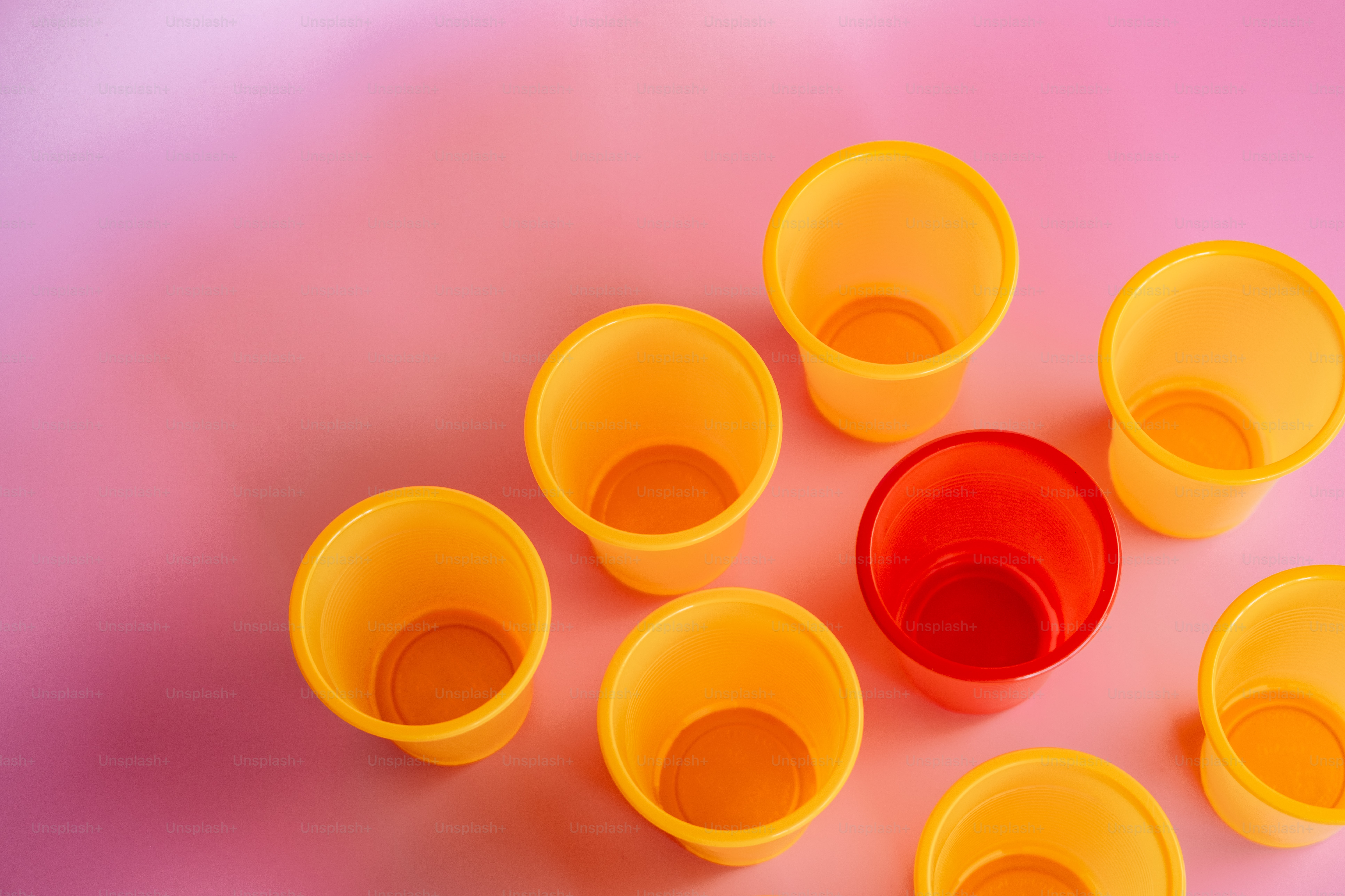 Acht Plastikbecher stehen auf einer rosafarbenen Fläche.