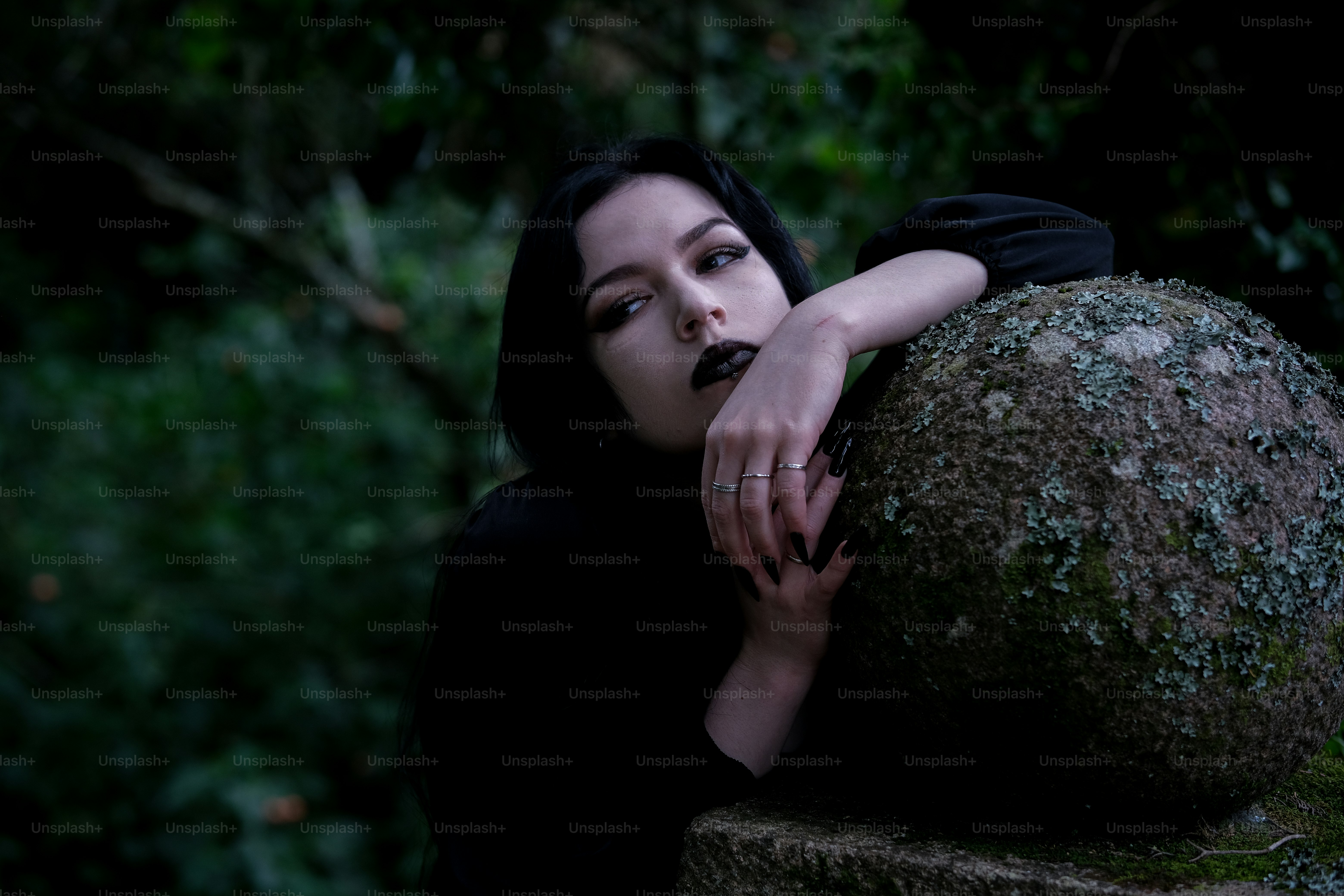 Uma mulher de cabelos escuros se apóia em uma pedra.