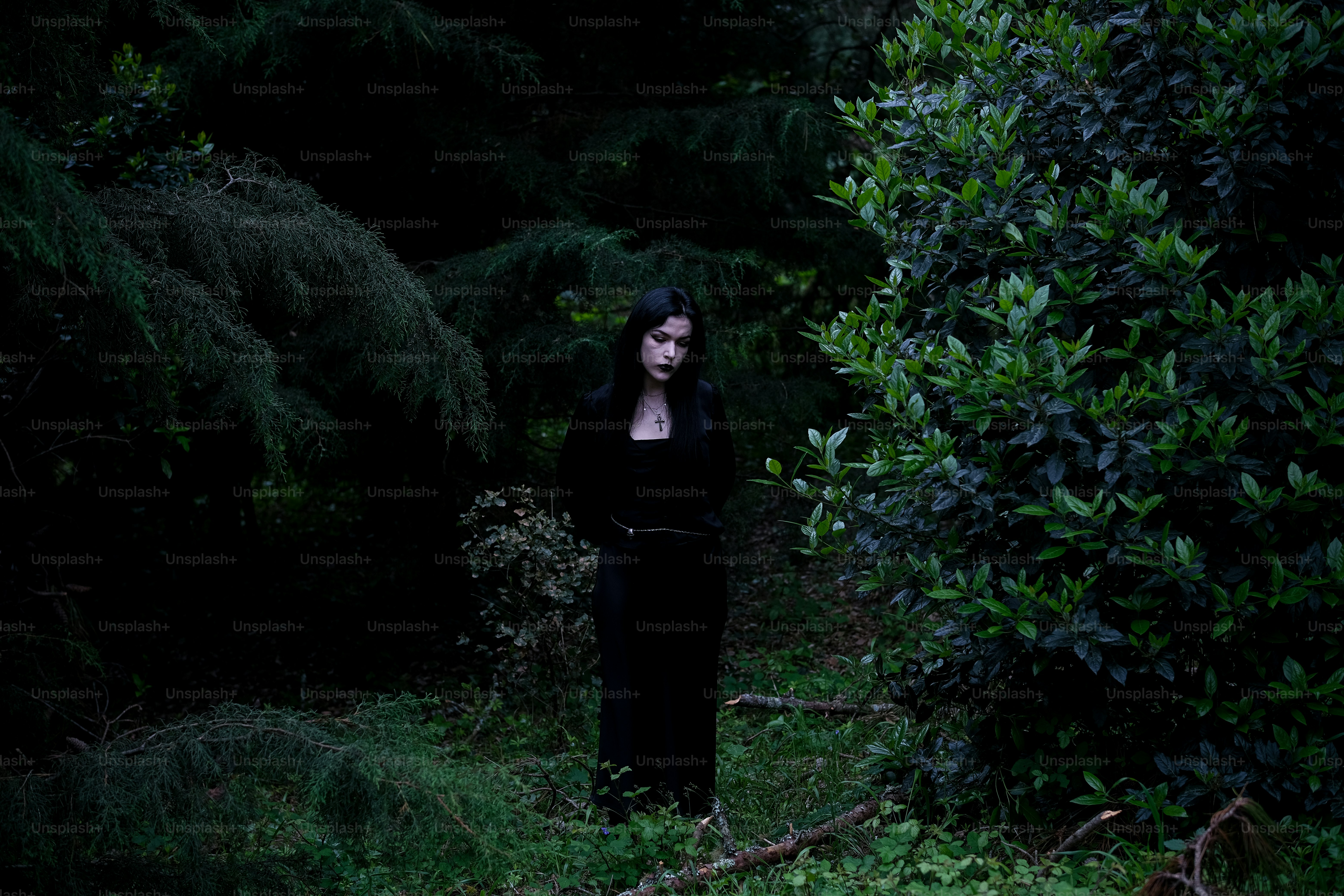 Mulher de preto fica em uma floresta escura.