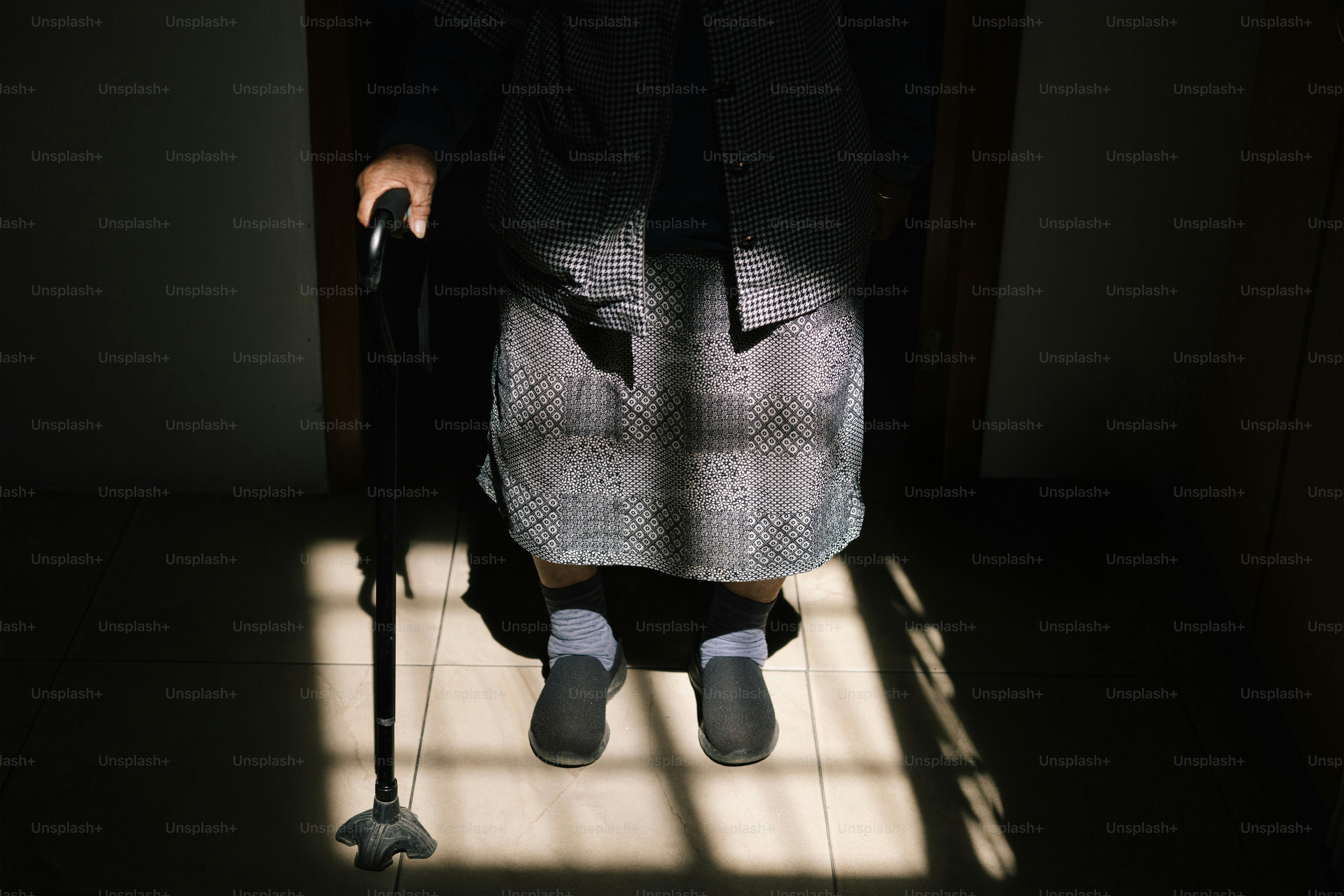 Una persona mayor está de pie en la puerta con un bastón.