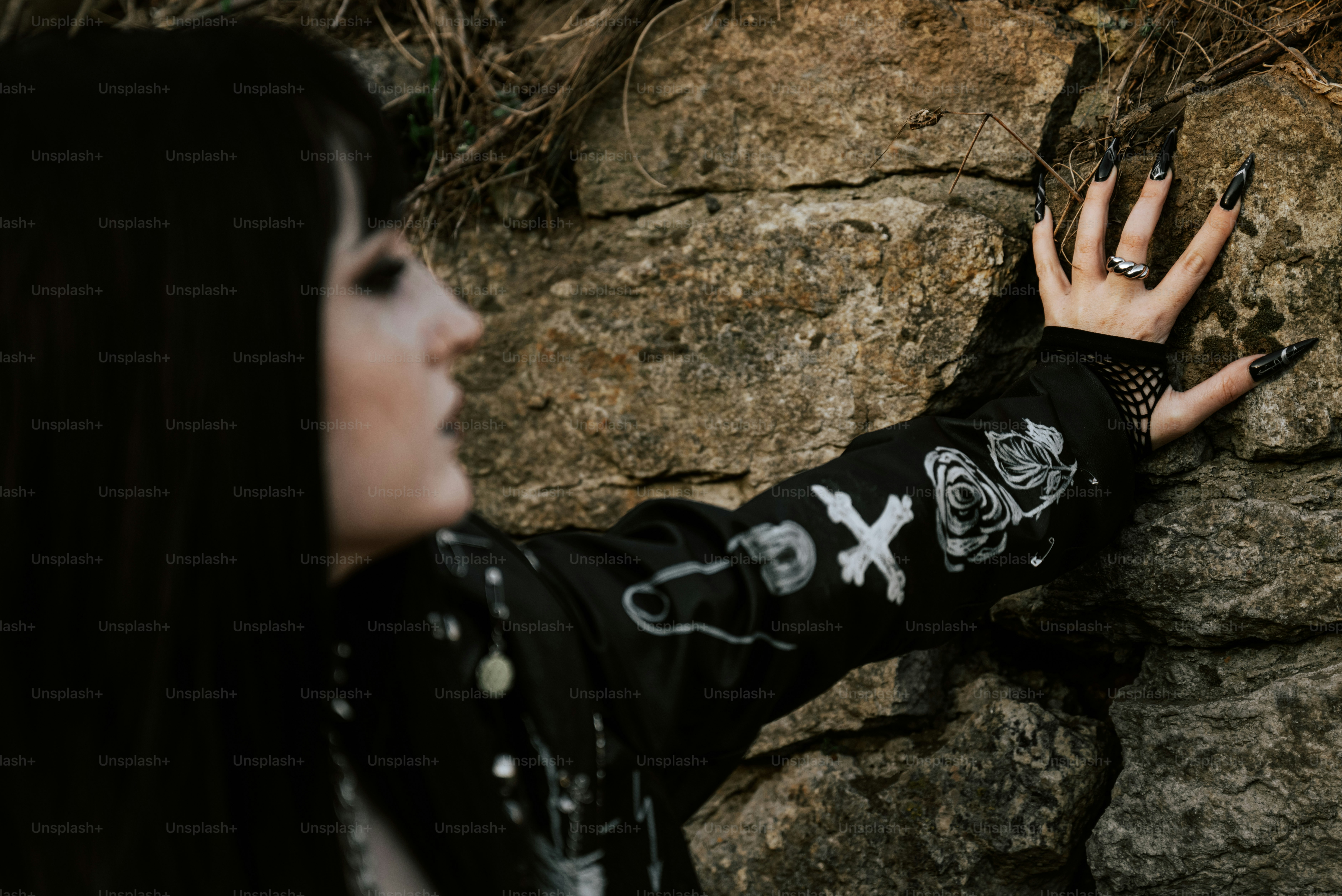 Woman with black nails and sleeve touches a stone wall.