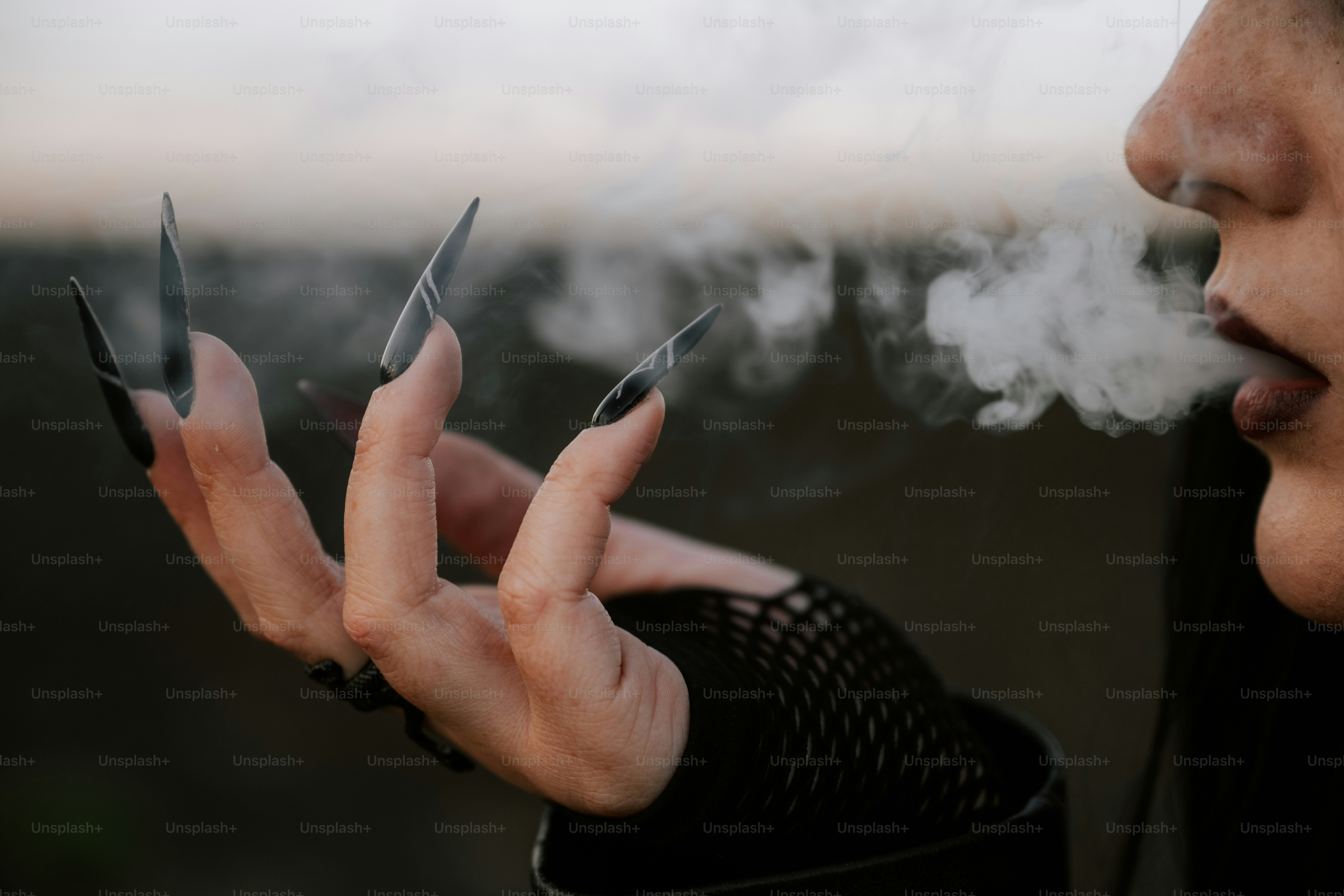 A person with long nails exhales smoke.