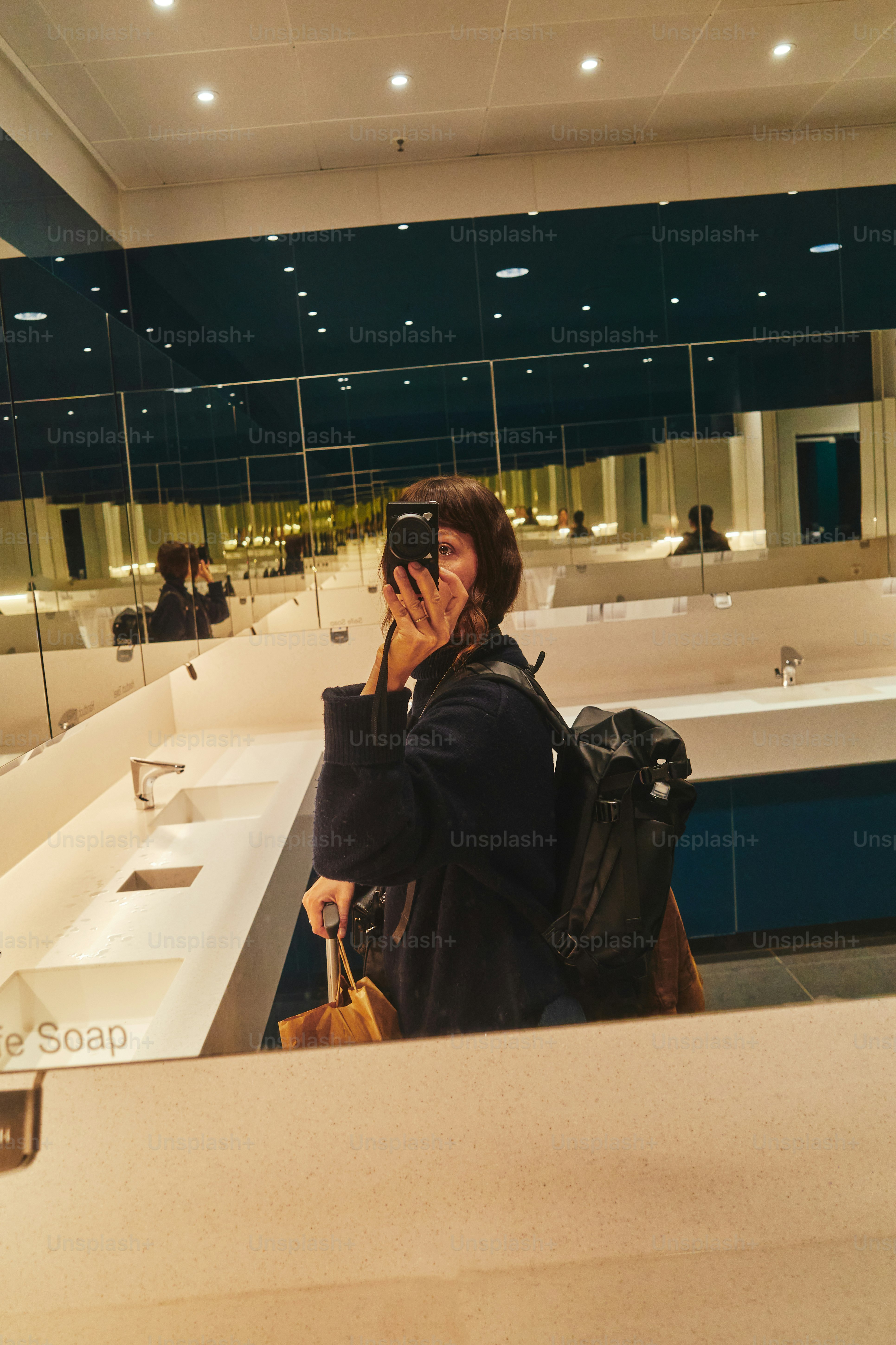 La persona si fa un selfie nello specchio di un bagno pubblico.