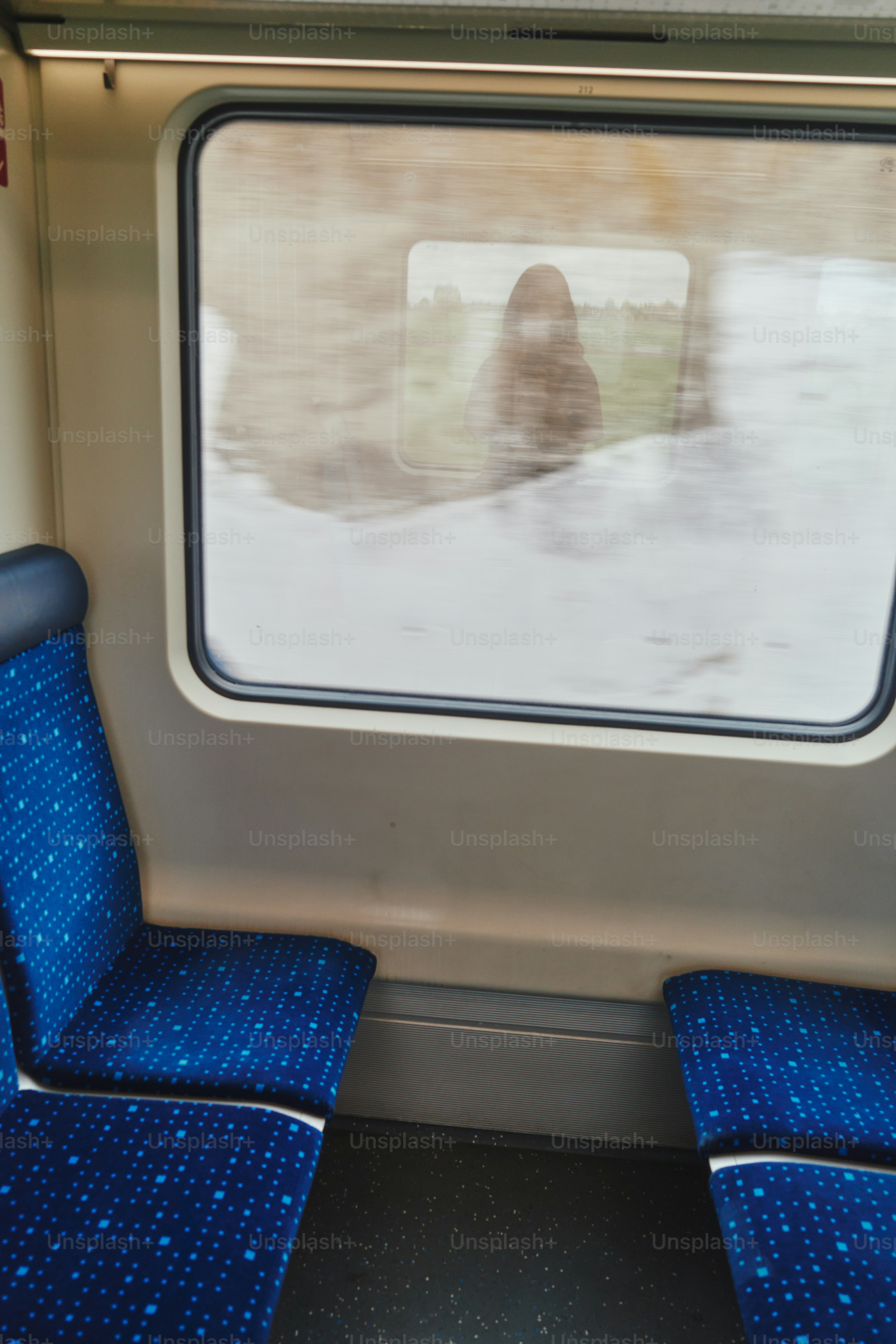 Di dalam kereta dengan kursi biru dan pemandangan kabur.