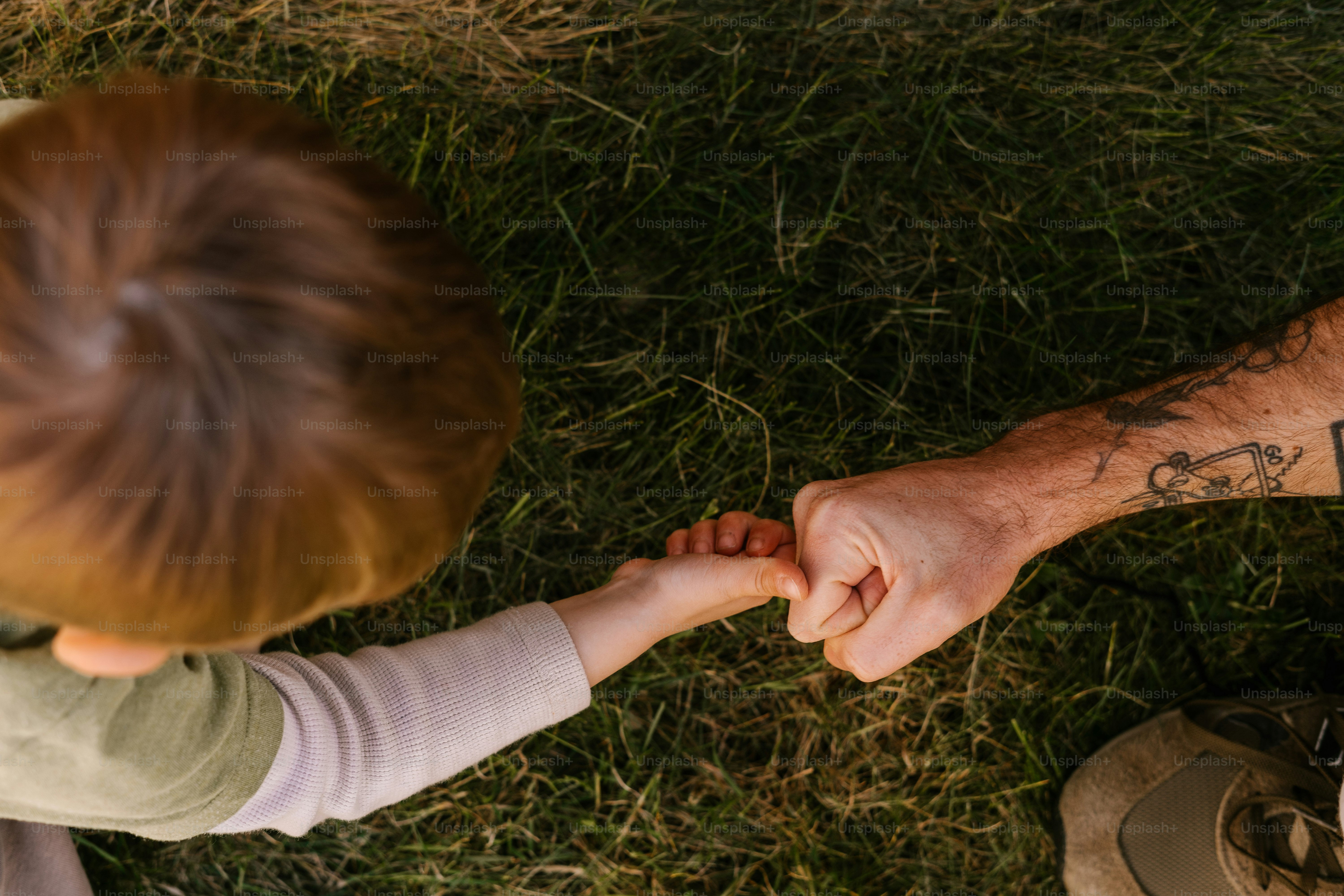 Child and adult bump fists in a grassy area.
