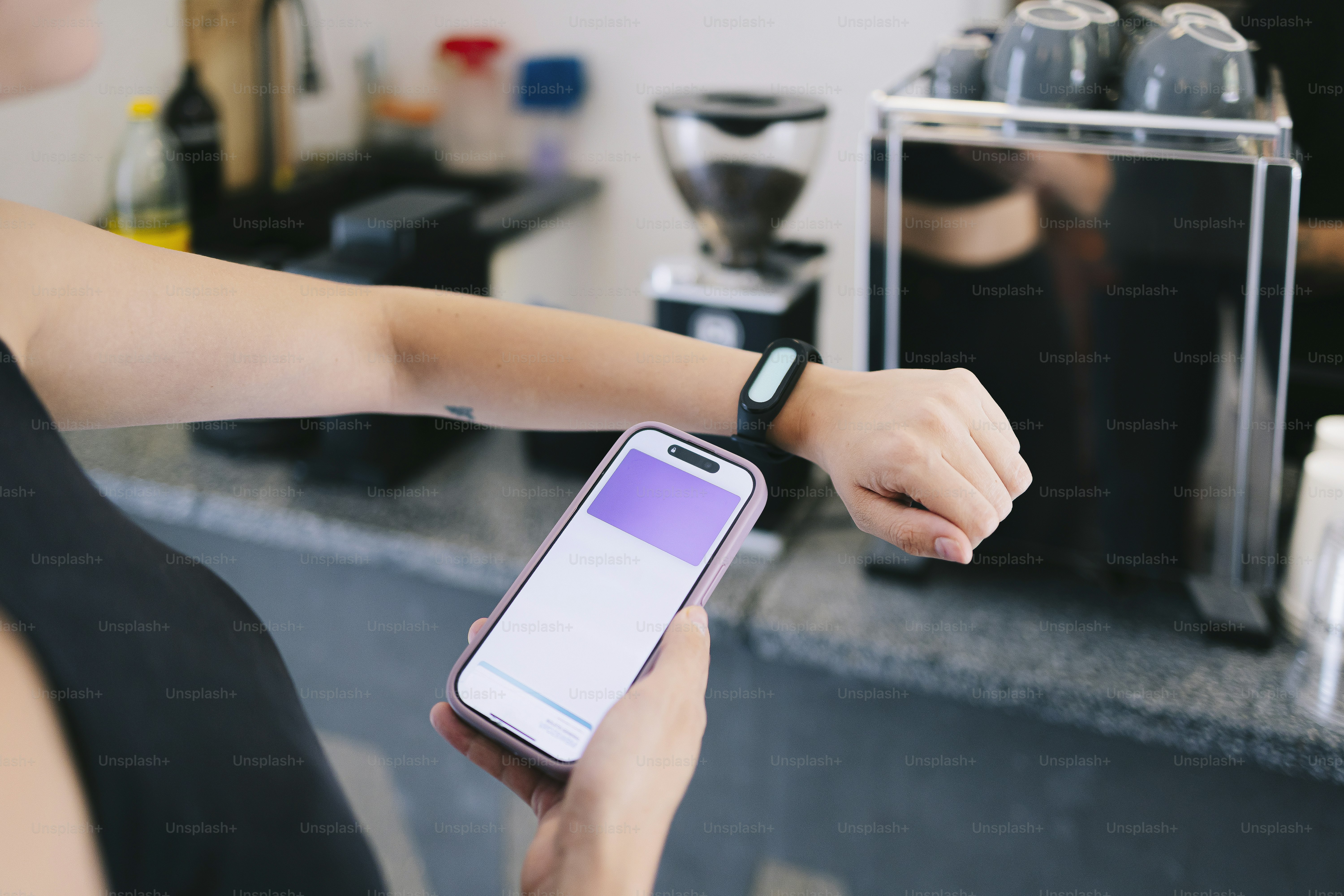 Uma pessoa verifica o telefone e o smartwatch perto da máquina de café.