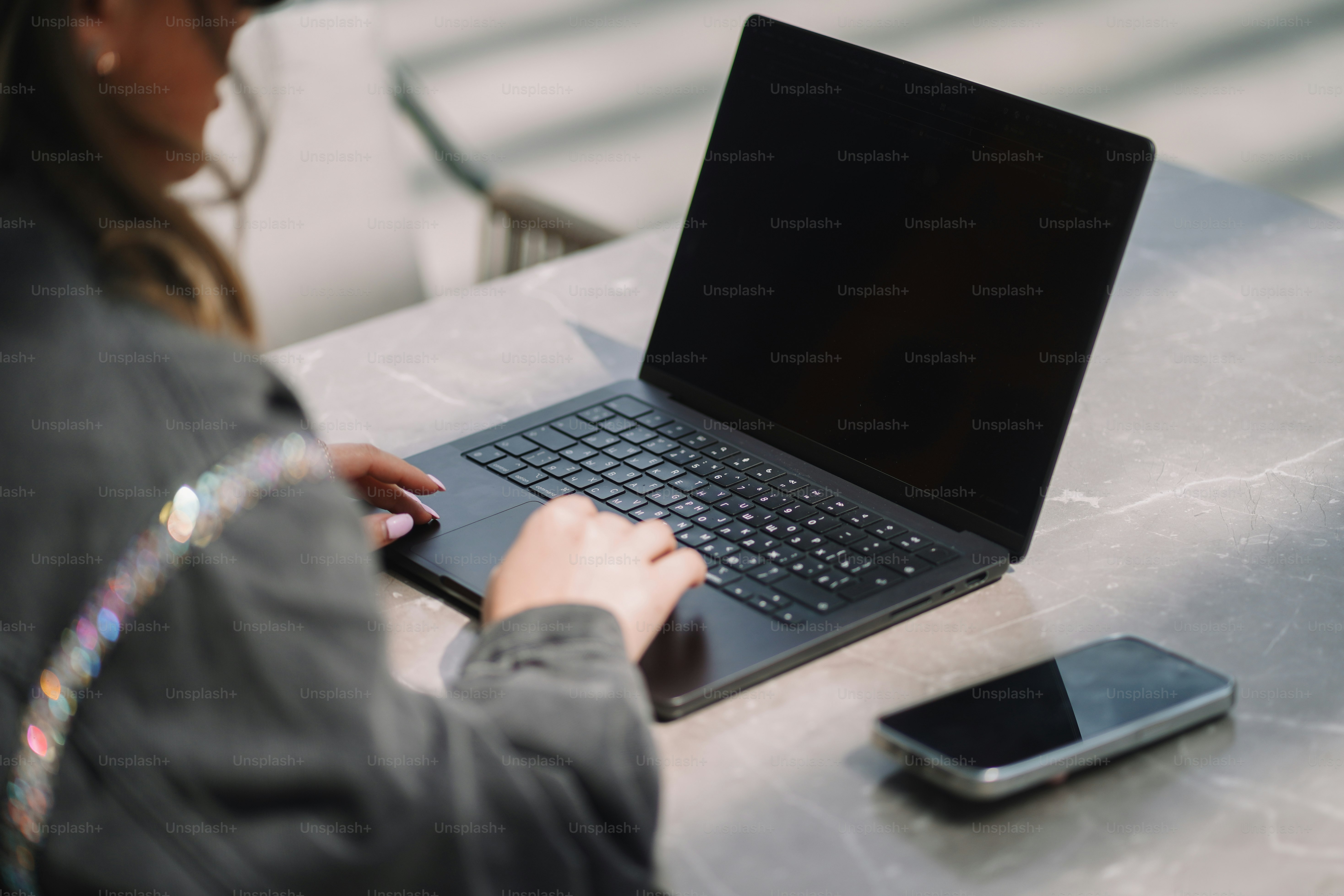 Woman works on a laptop with a phone beside it.