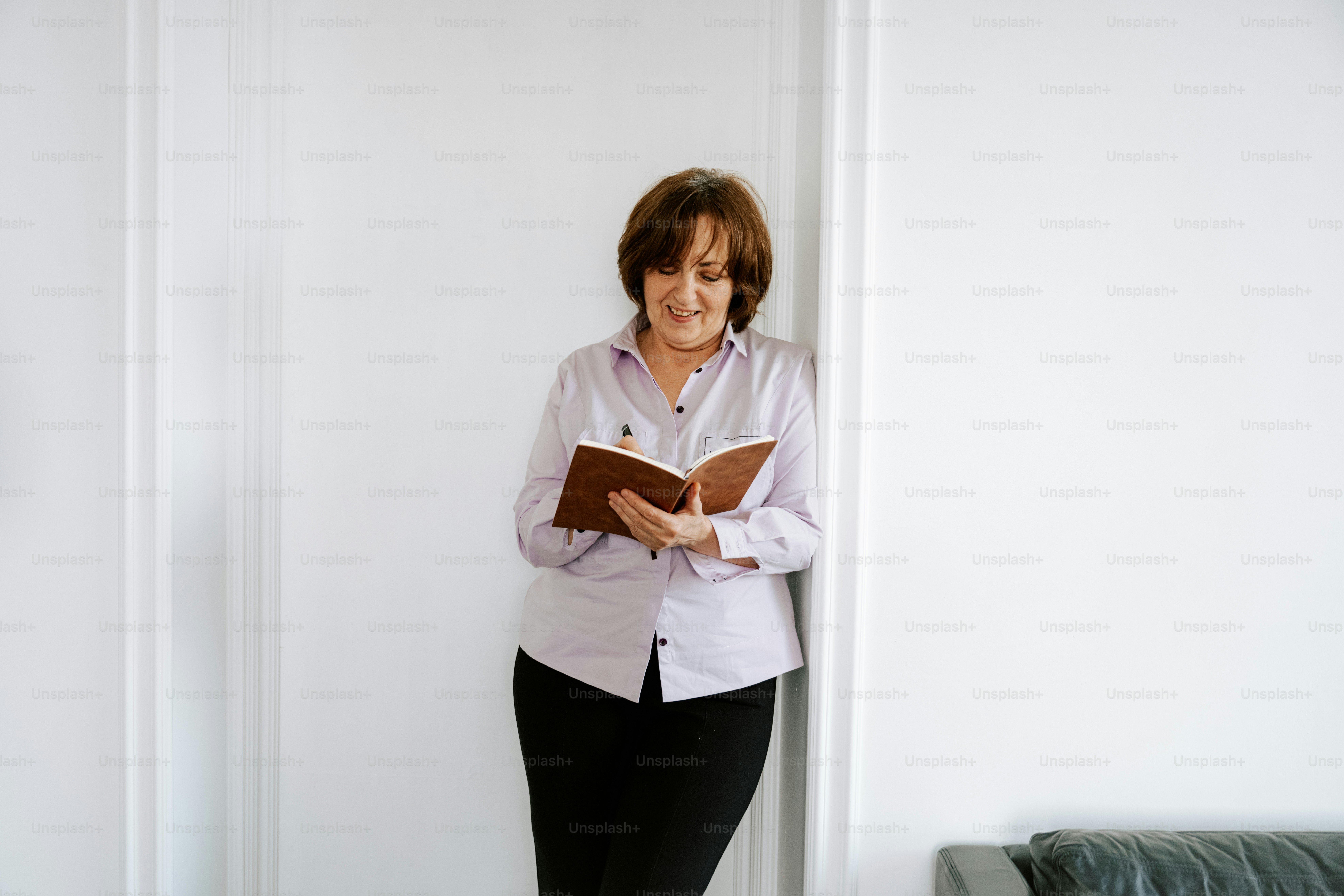 A woman reads a book against a white wall.