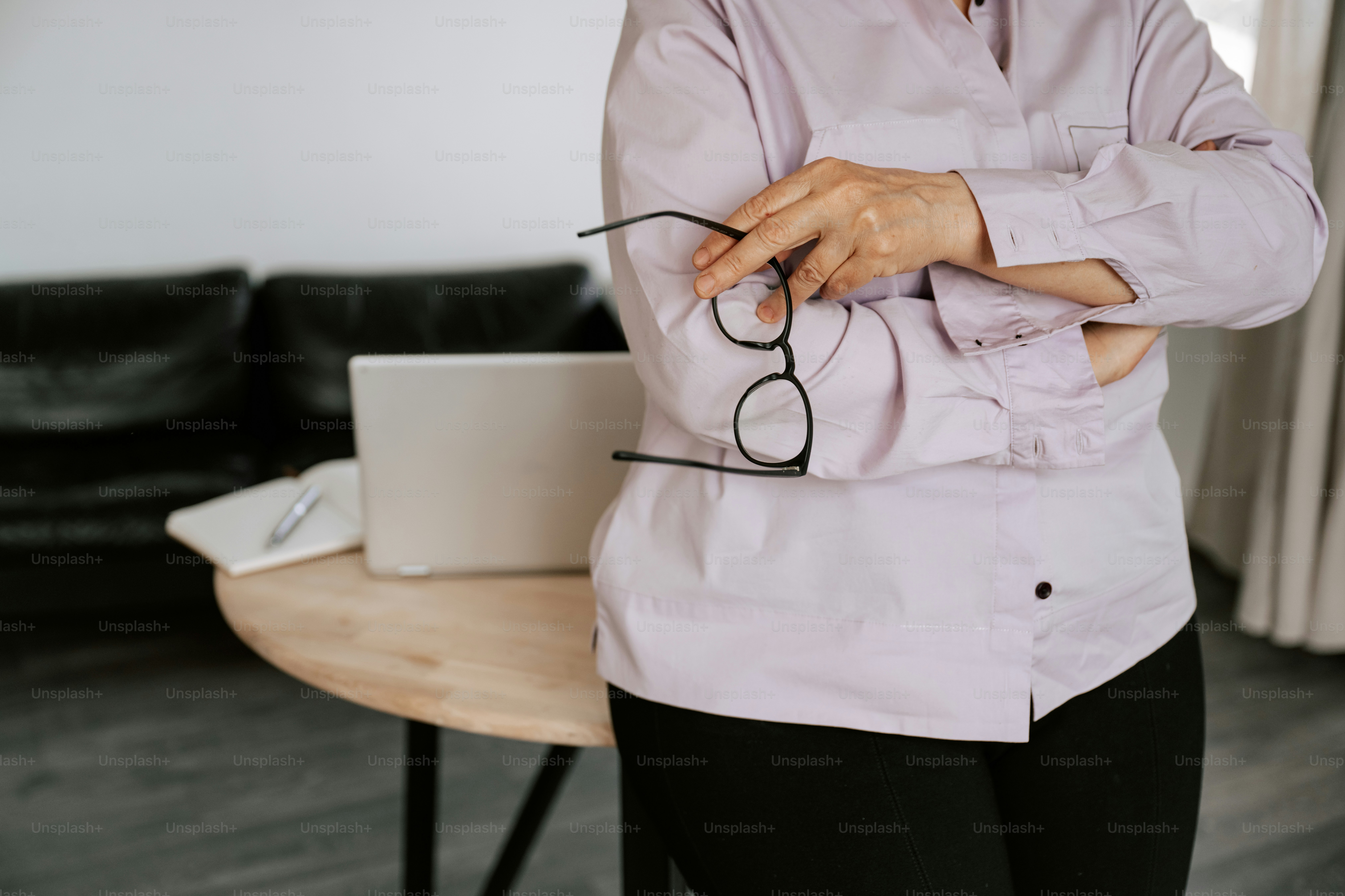 Woman holding glasses stands near a laptop.