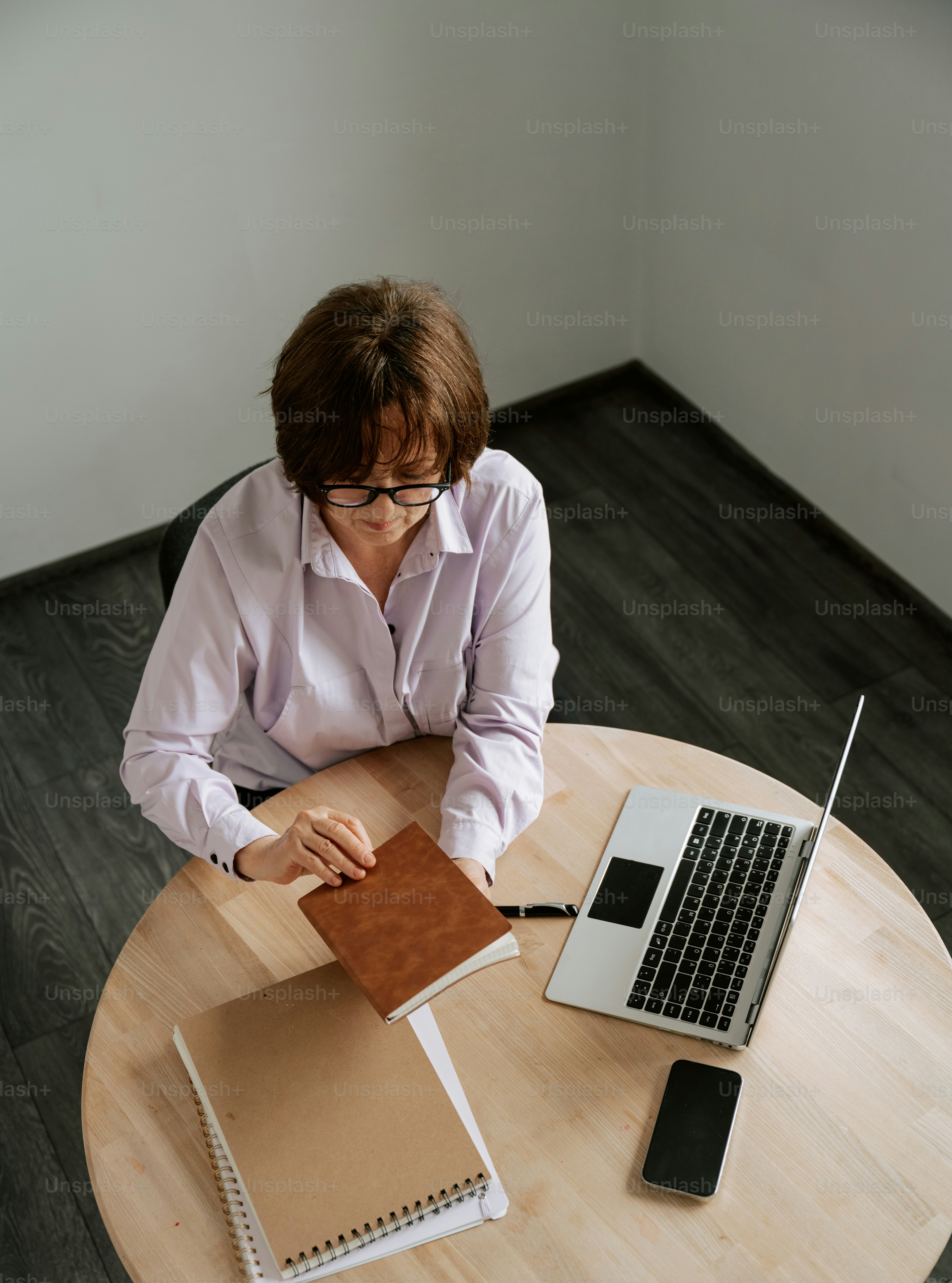 Woman works on a laptop, taking notes in a journal.