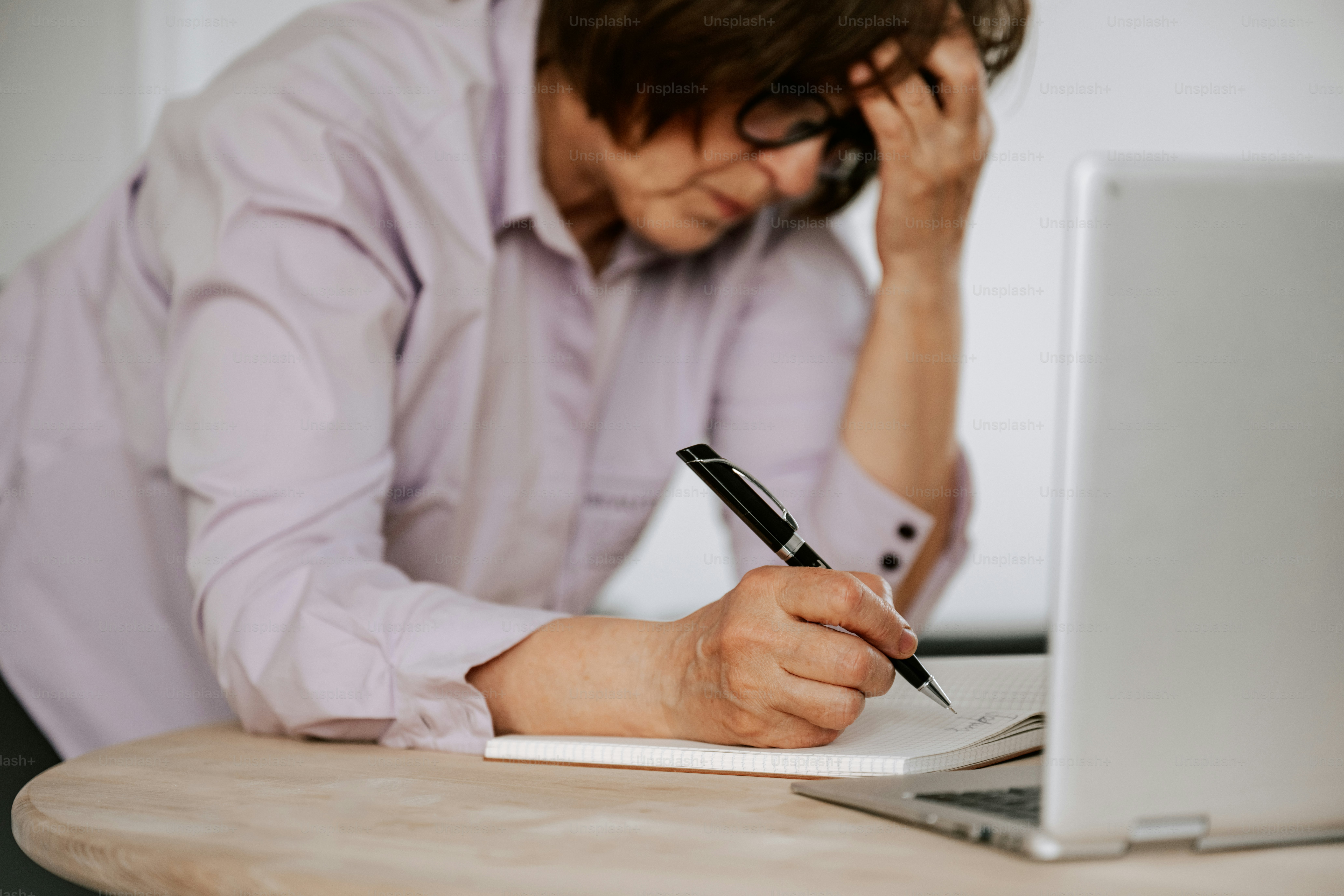 Woman appears stressed while writing and using a laptop.