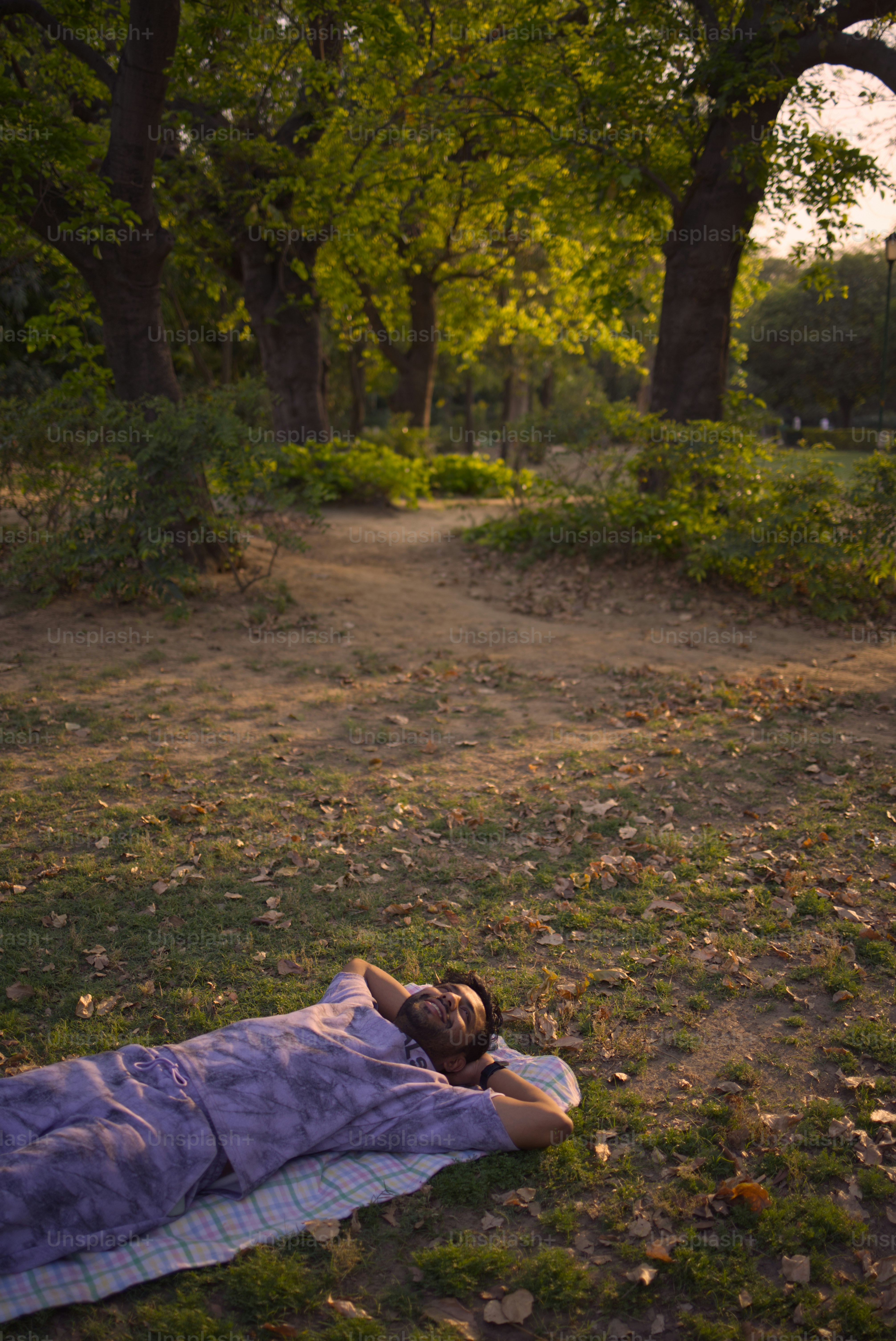 Man relaxes on a blanket in a sunlit park.