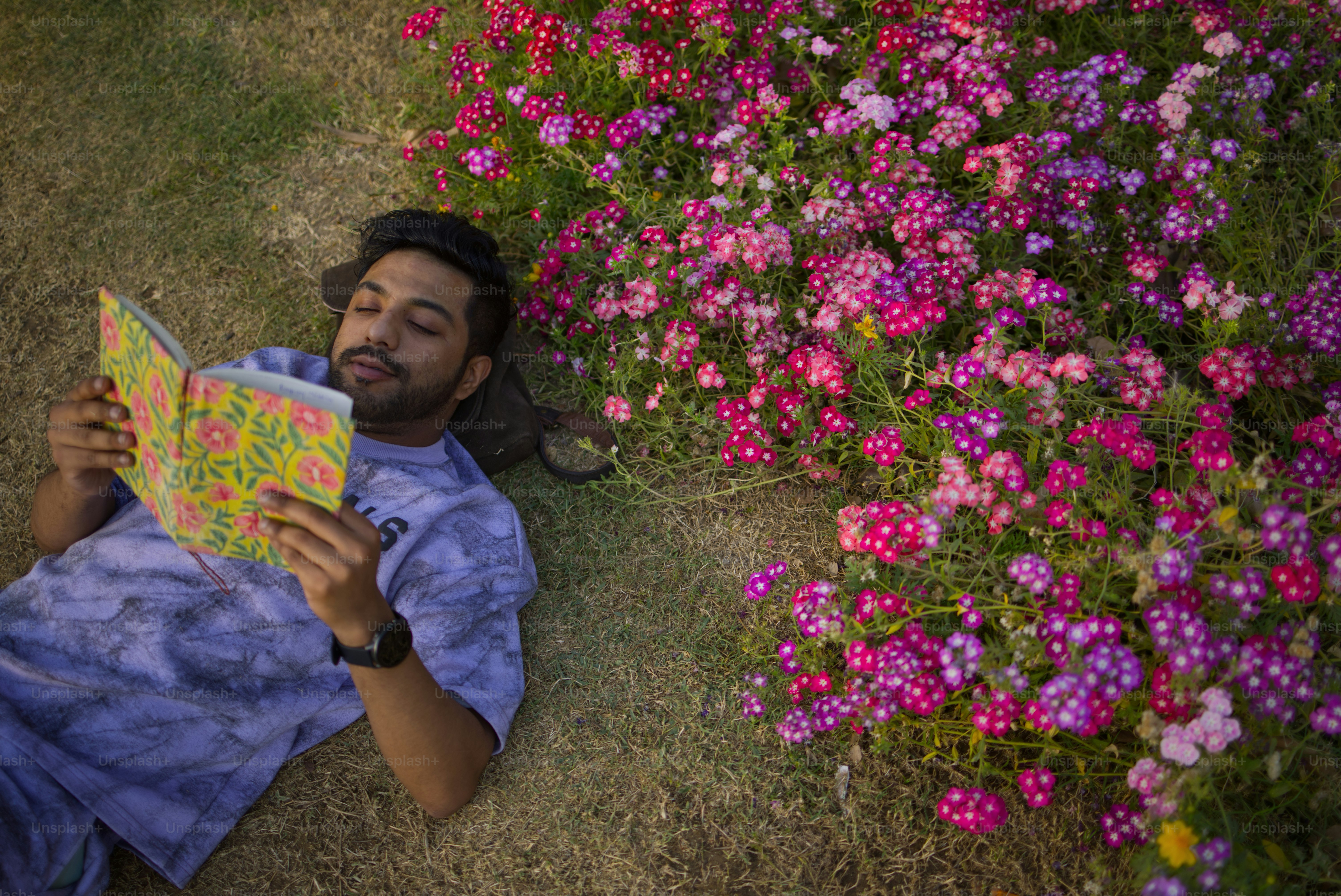 A man reads a book in a flower garden.