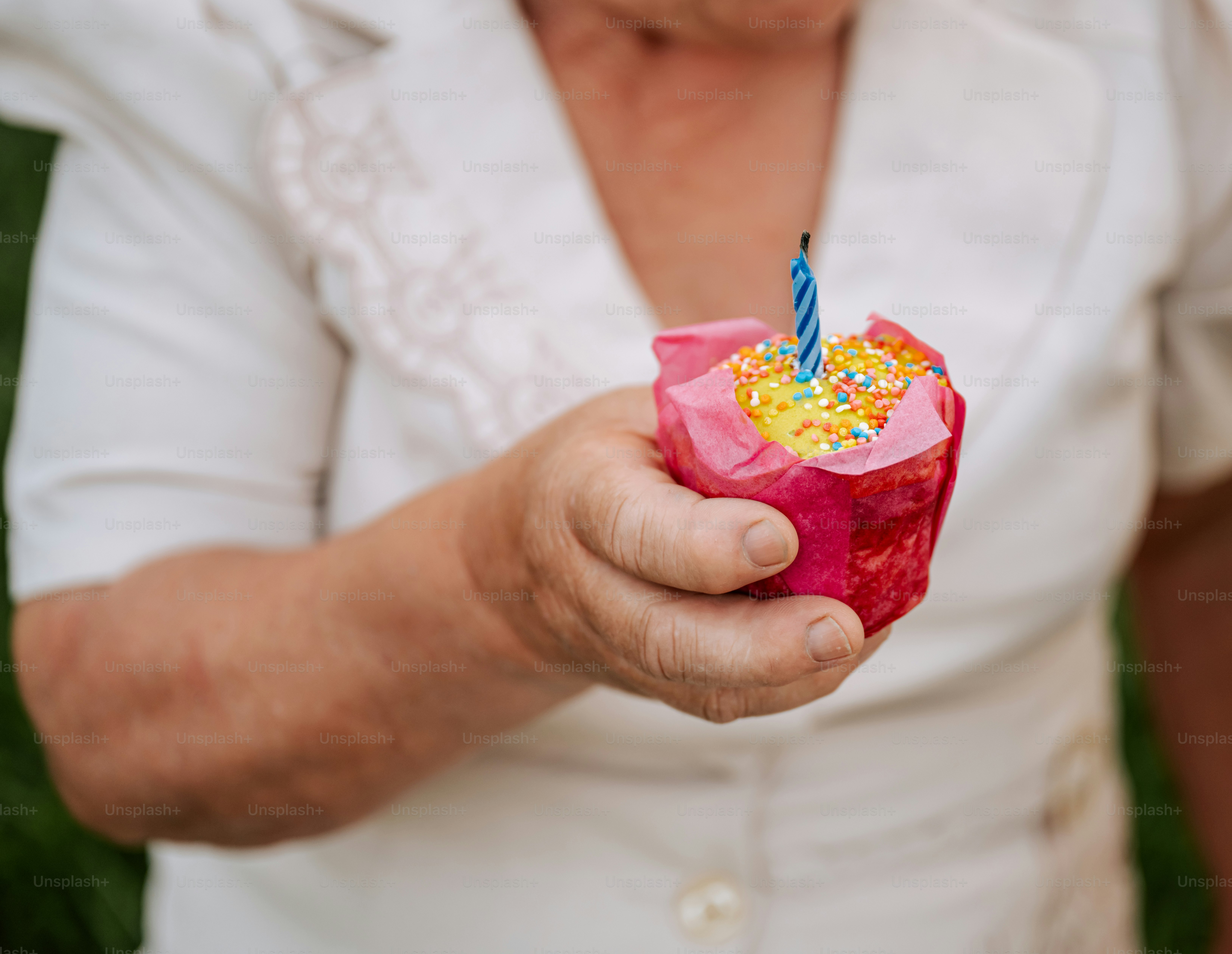 Eine Frau hält einen Cupcake mit einer brennenden Kerze in der Hand.