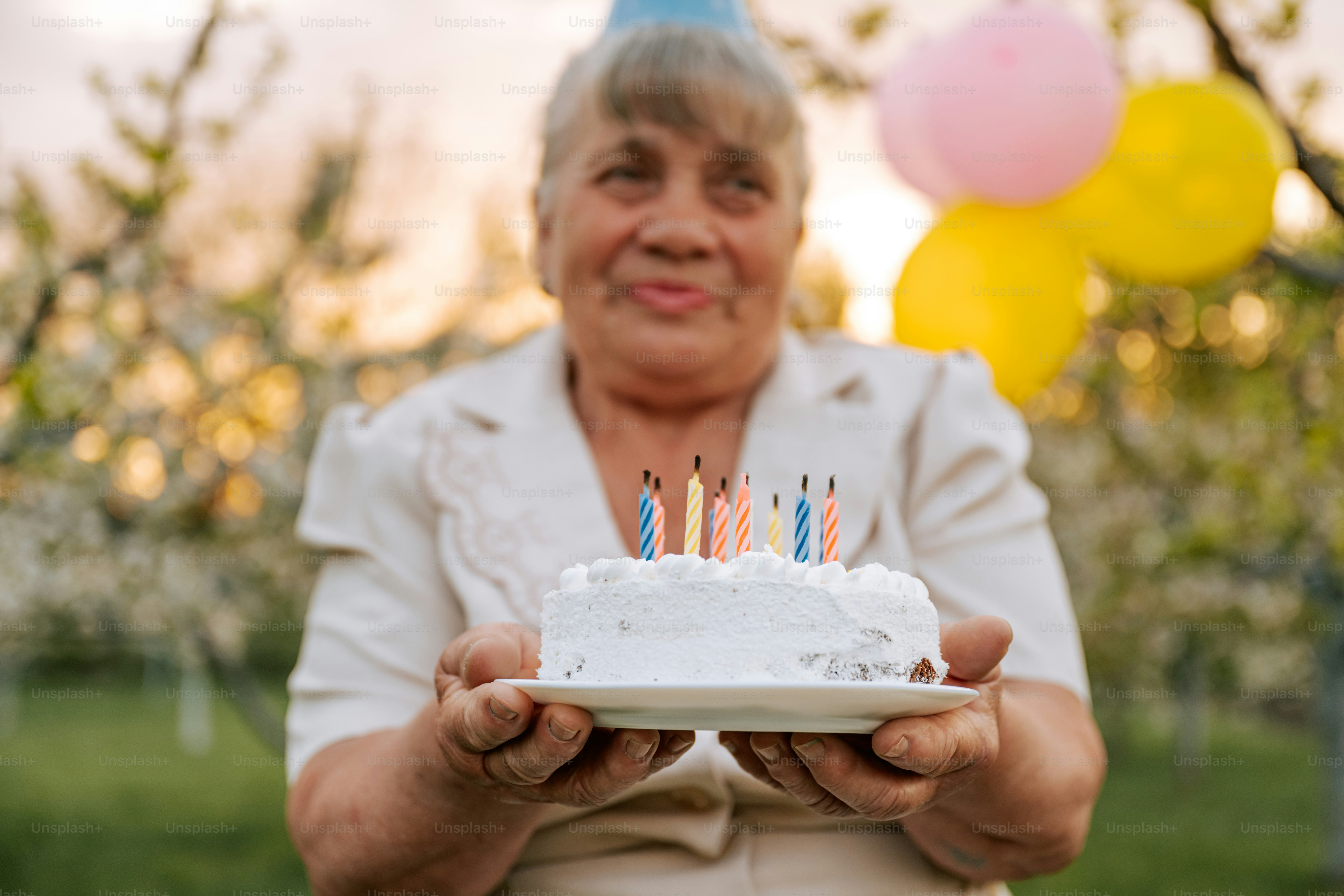 Frau hält einen Geburtstagskuchen mit brennenden Kerzen.