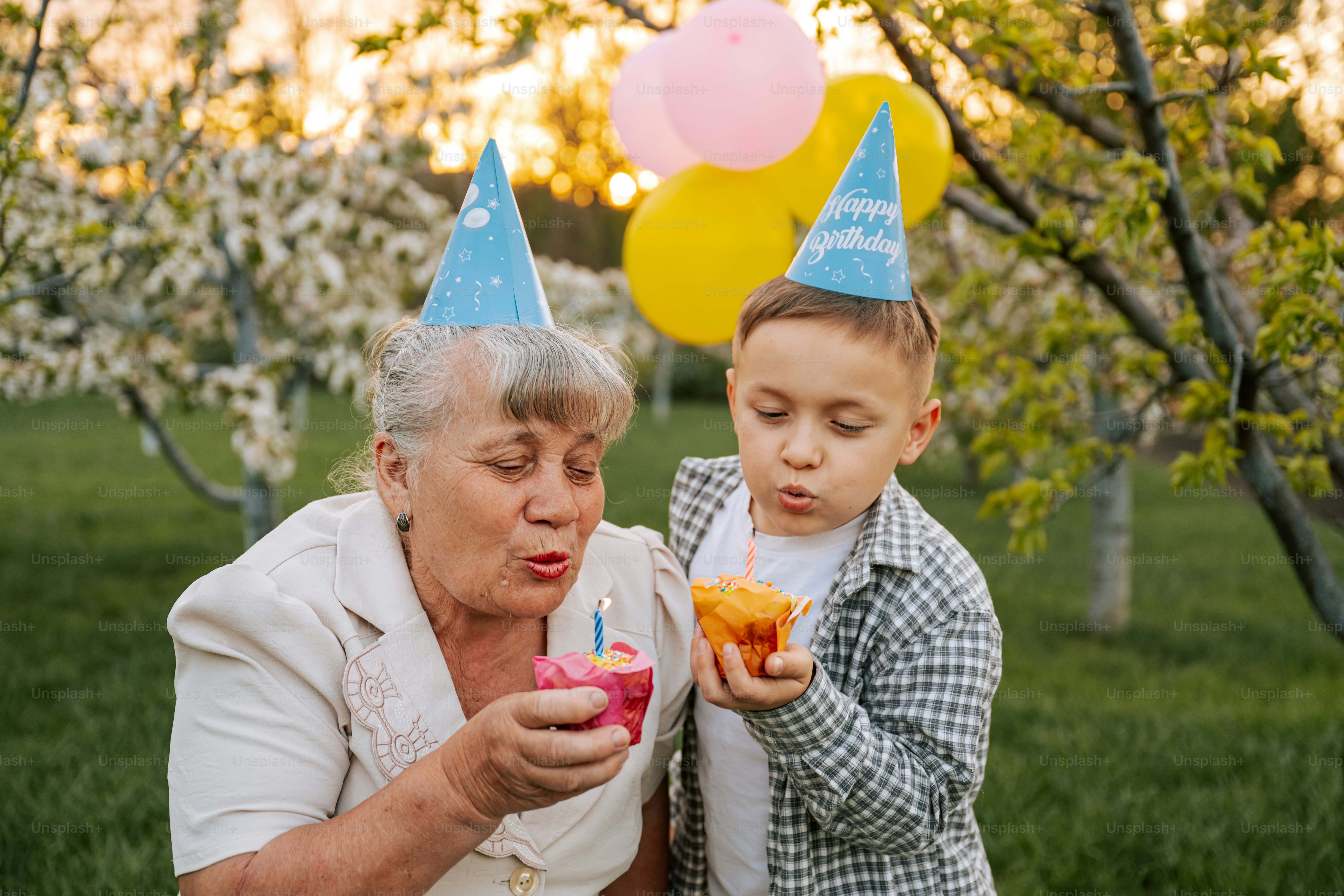 Oma und Enkel blasen Kerzen auf Cupcakes aus.