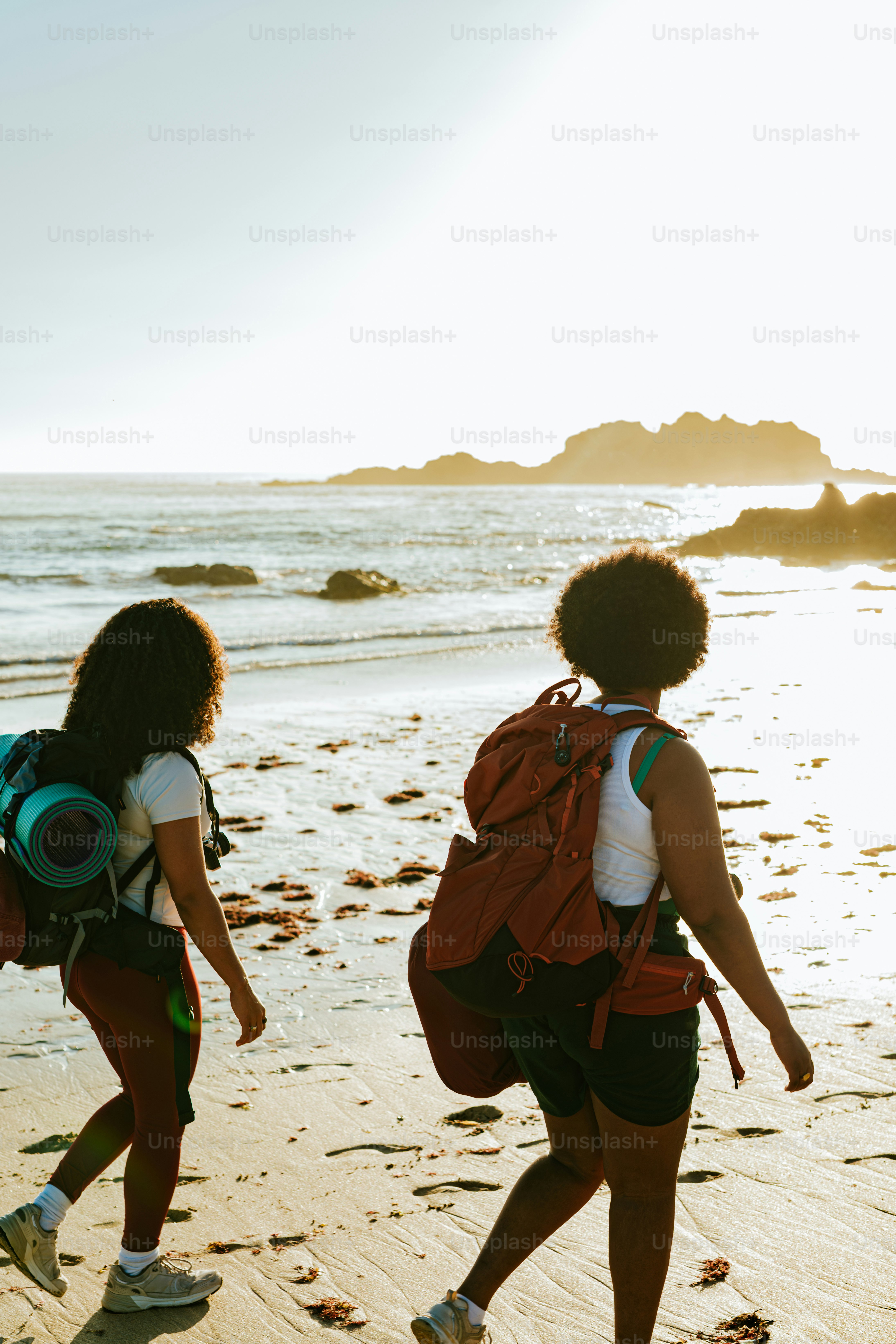 Two backpackers hike along a sunny beach.