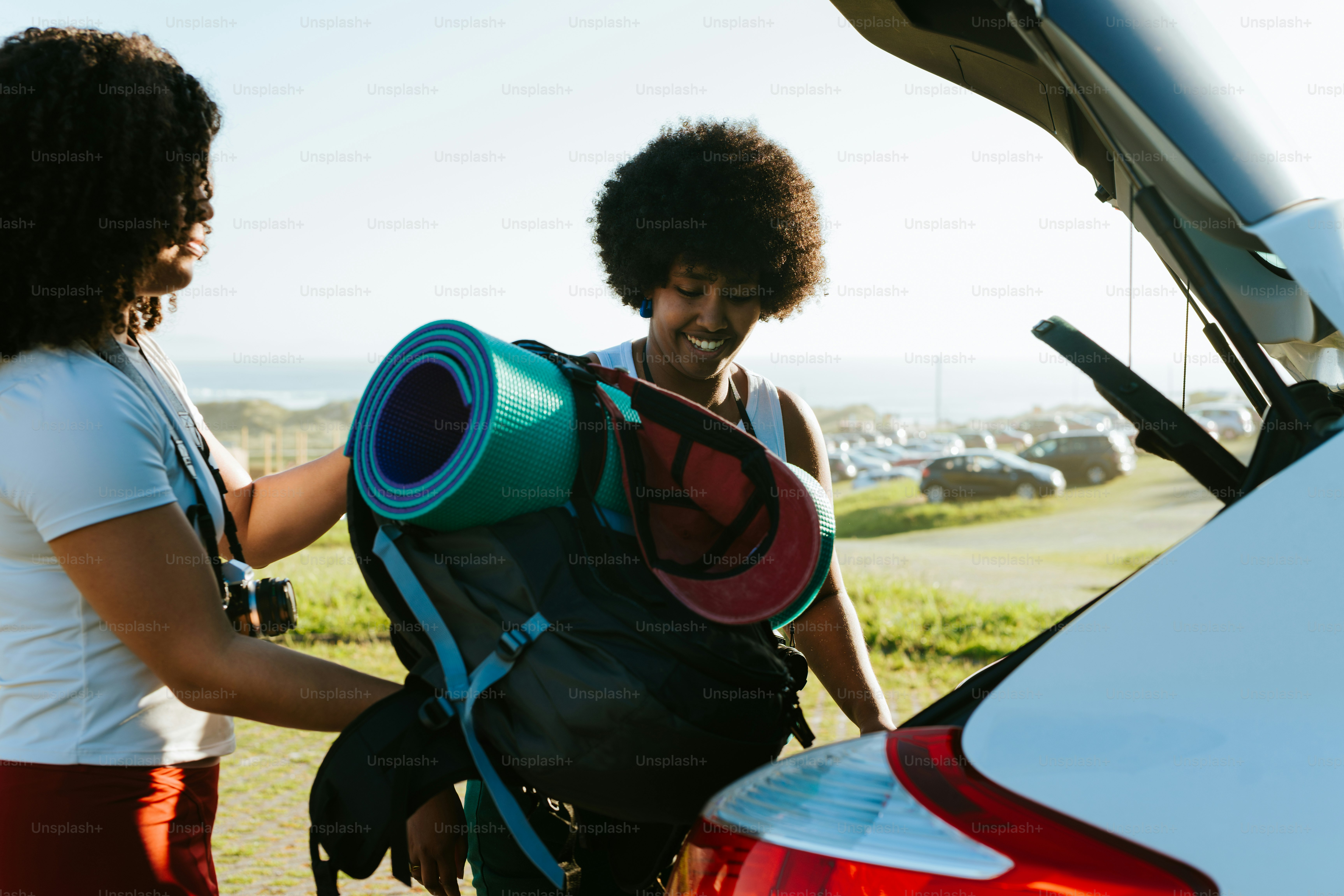 Friends happily pack a car with camping gear.