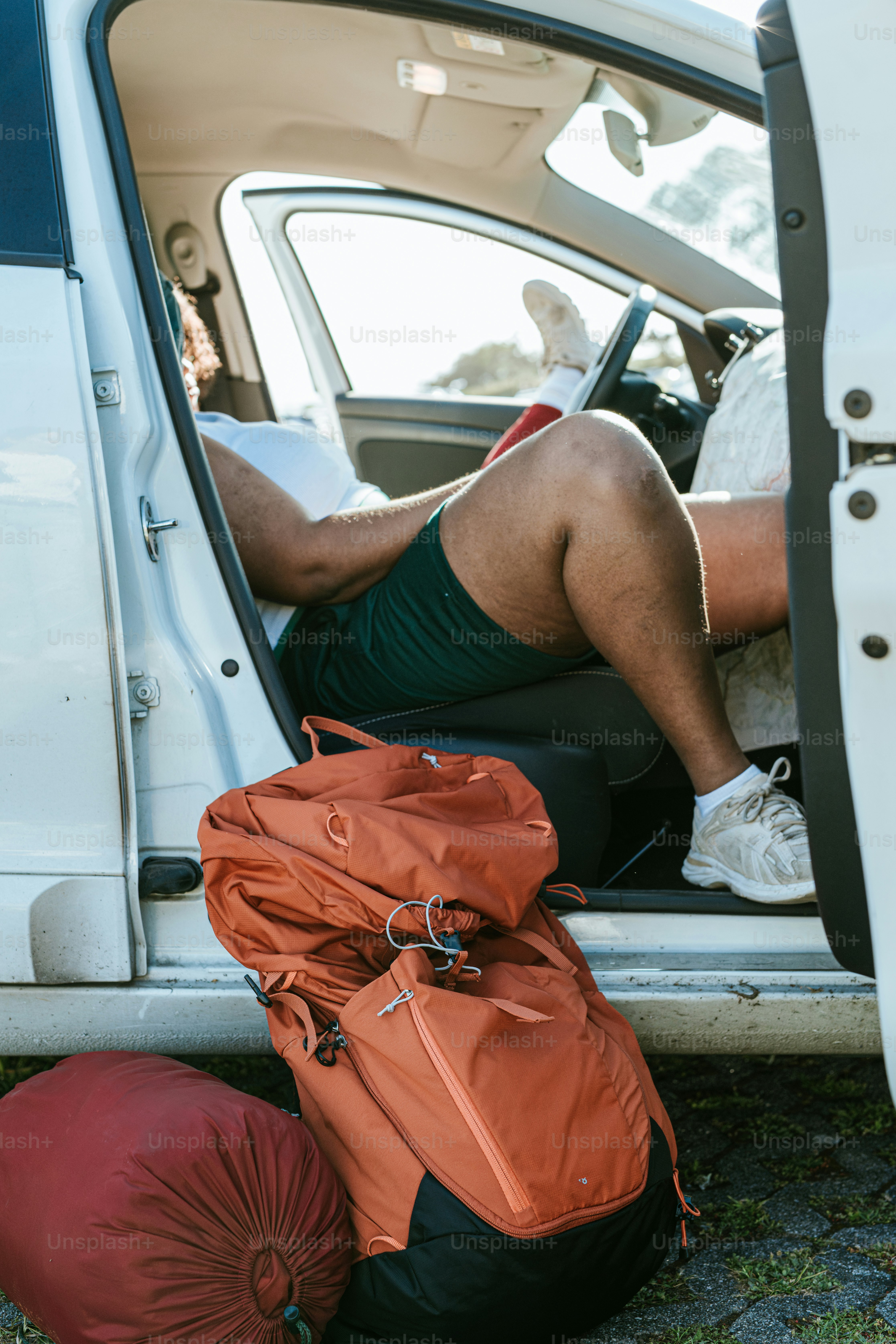 A person relaxing in a car with backpacks.