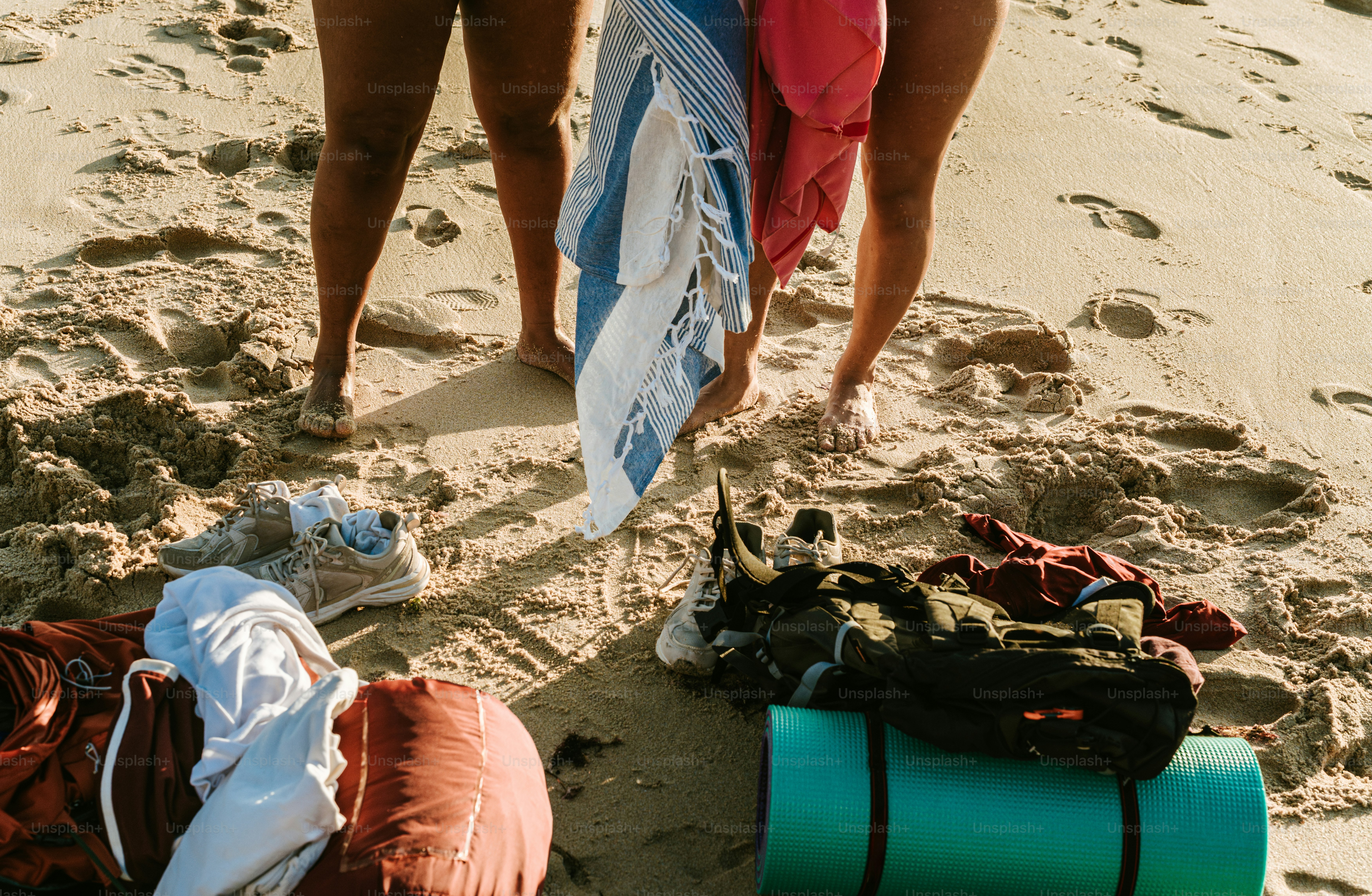Two people relax on a sandy beach with gear.