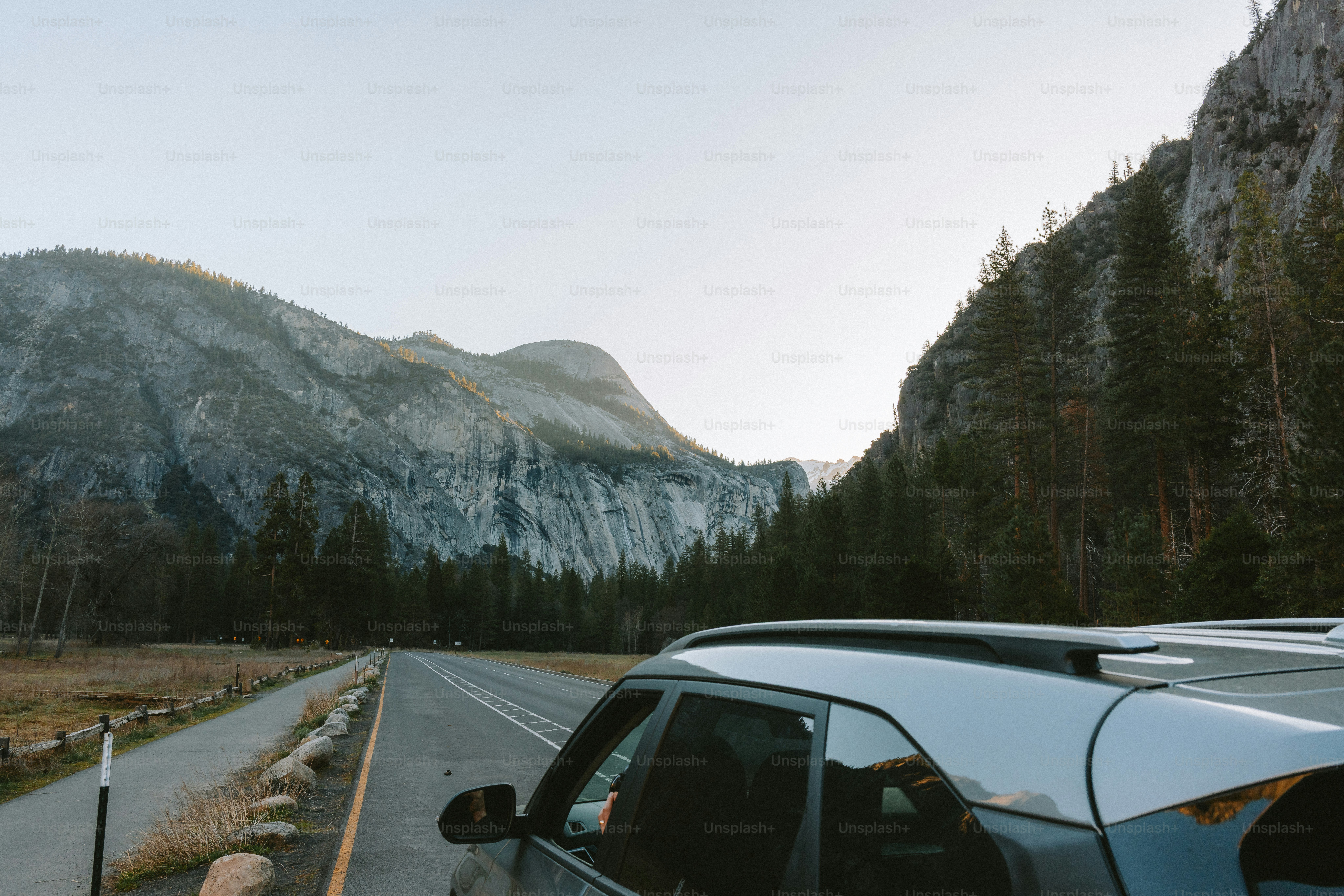 A car drives on a road by majestic mountains.