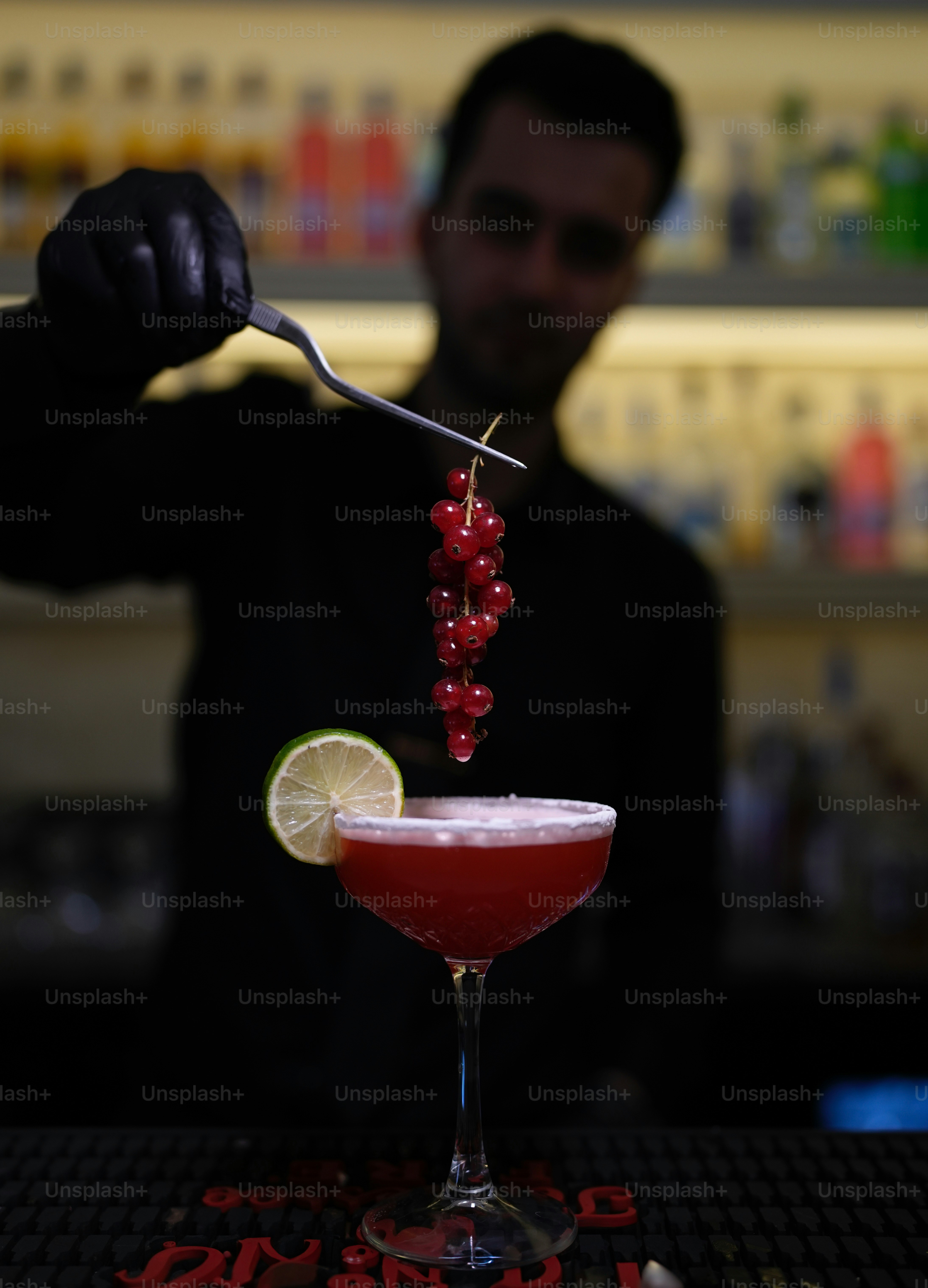 O barman enfeita um coquetel vermelho com frutas vermelhas.