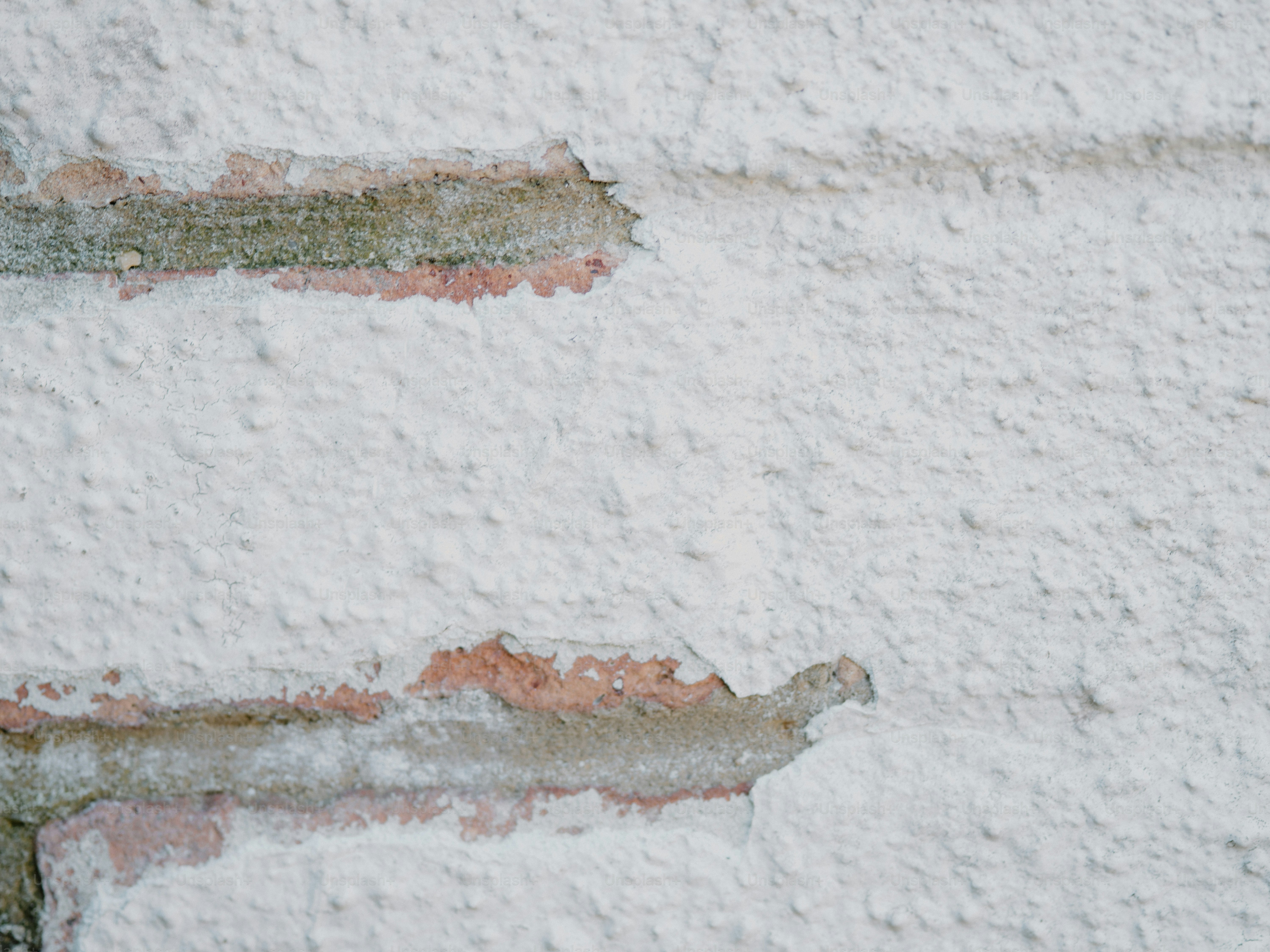 Beschädigte Ziegelwand mit abblätternder weißer Farbe.