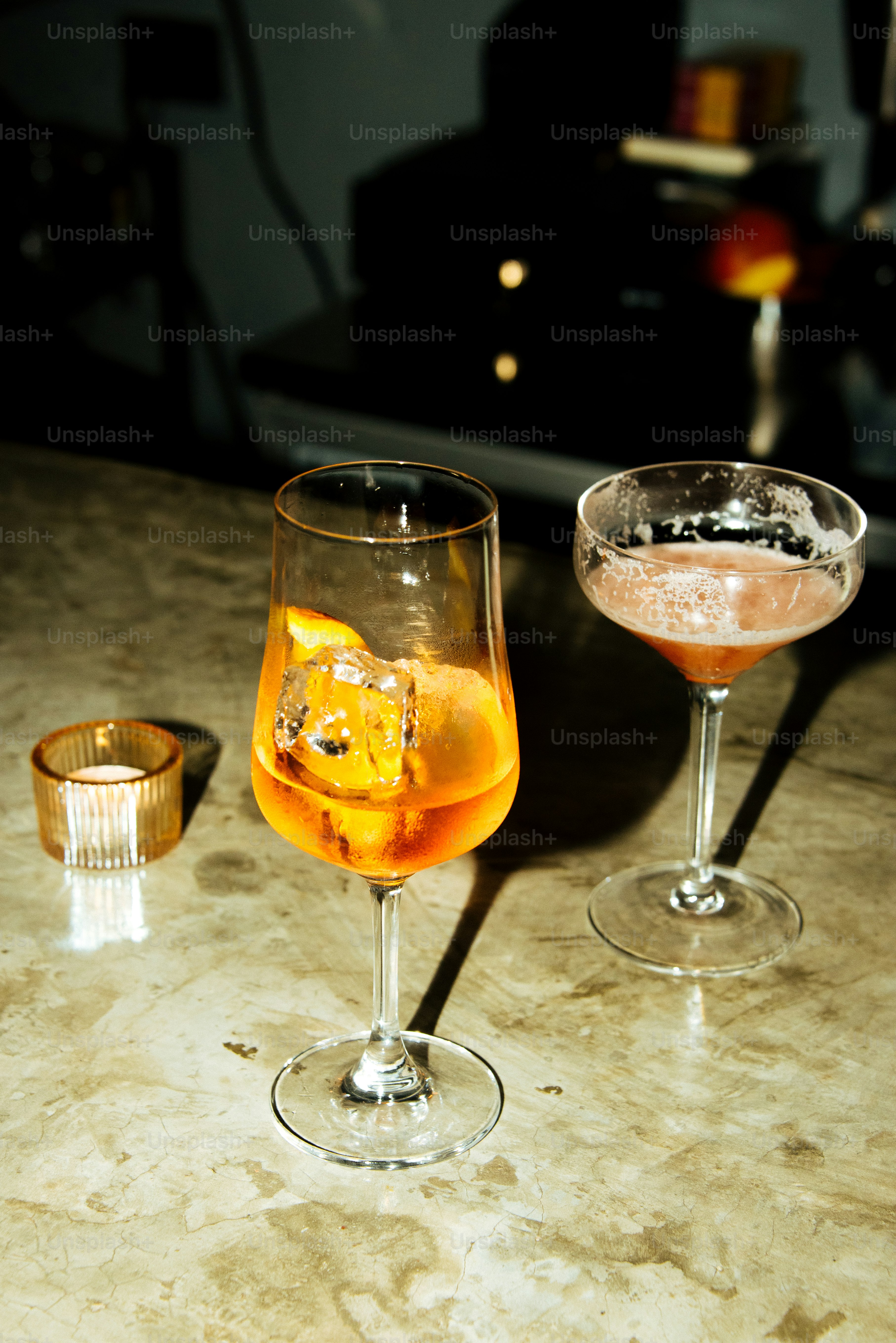 Two cocktails and a small candle are on a bar