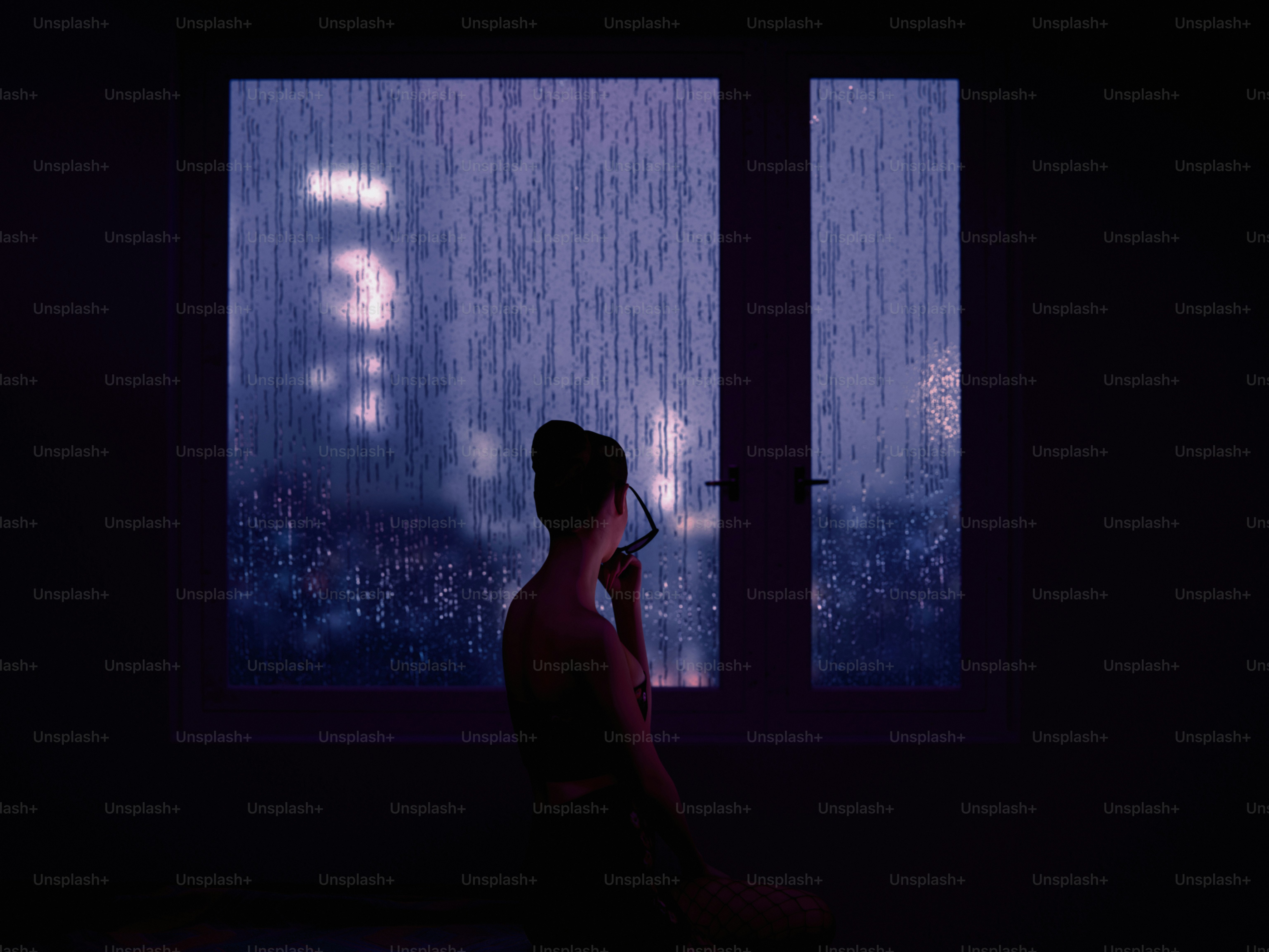 Woman gazes out a rainy window at night