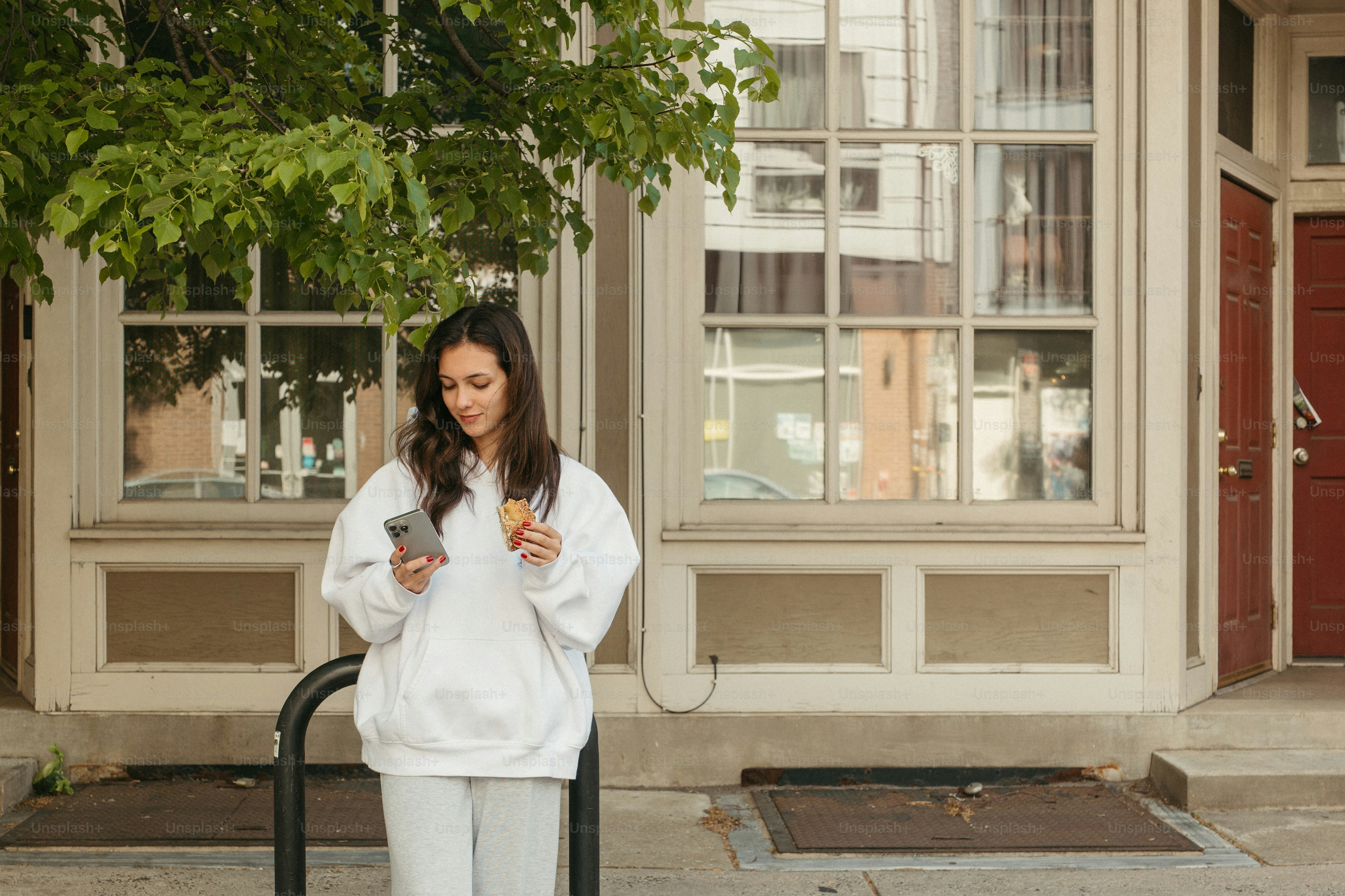 Woman in white holds phone and snack.