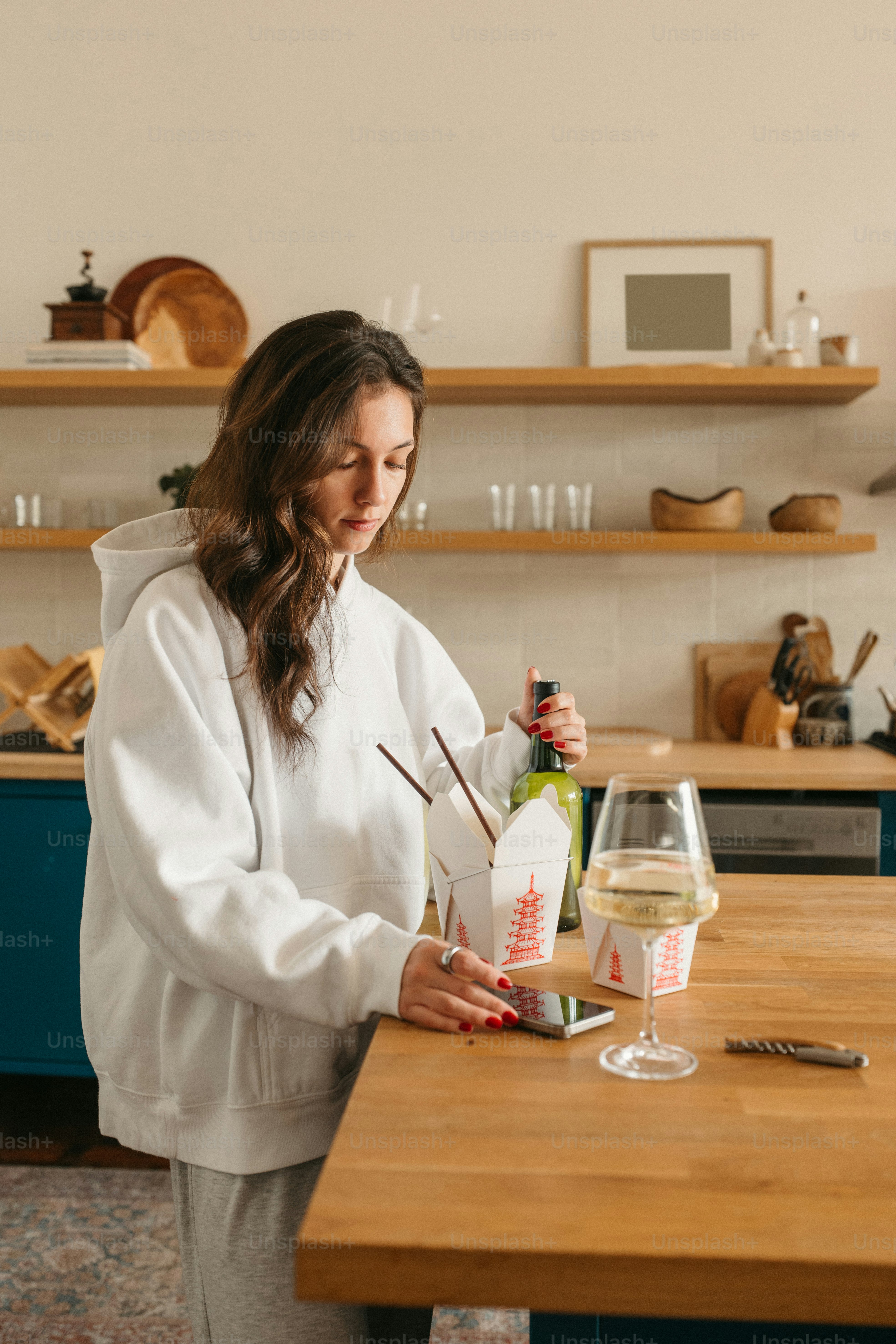 Woman prepares takeout food and wine at home.