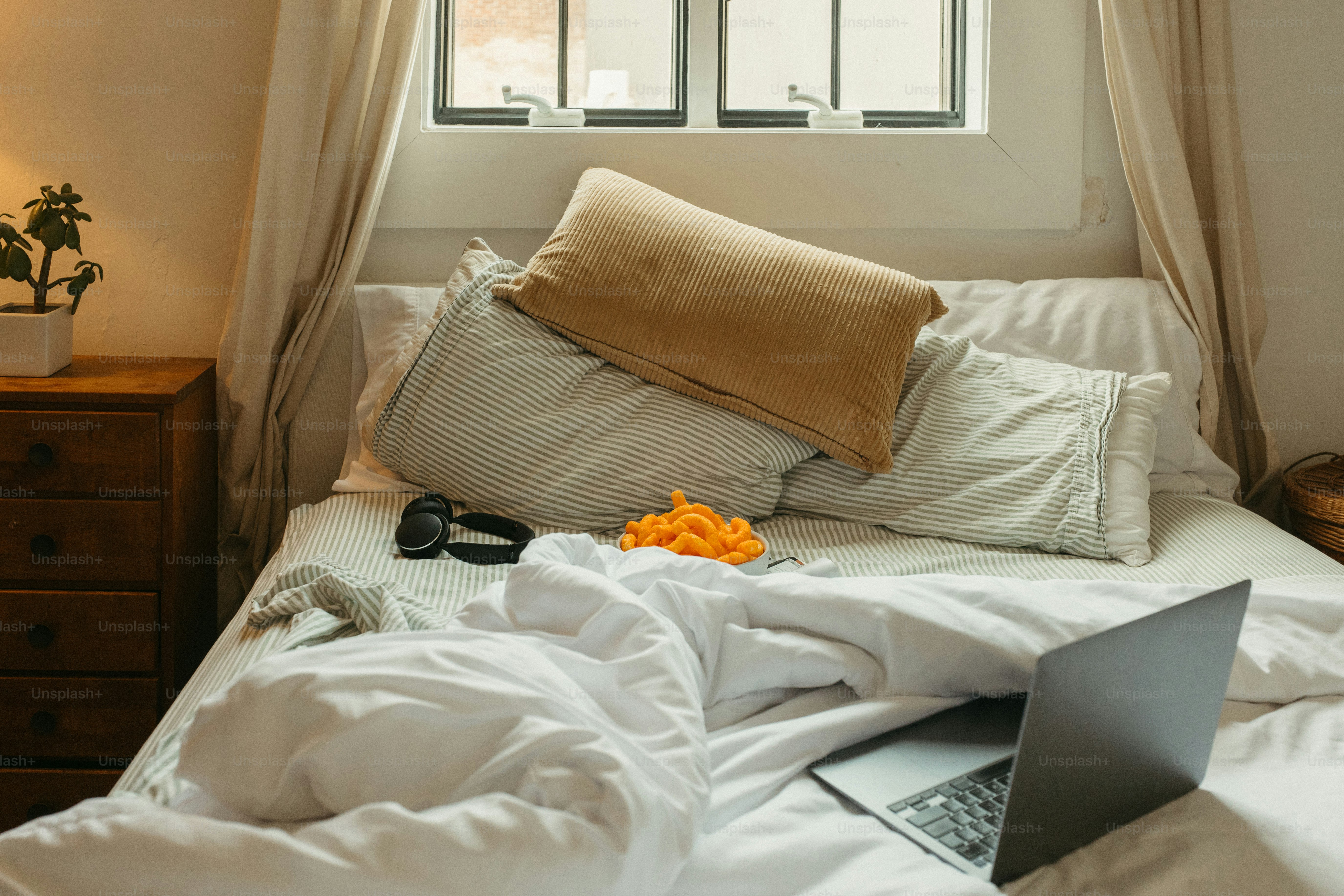 Unordentliches Bett mit Laptop, Kopfhörern und Kissen.