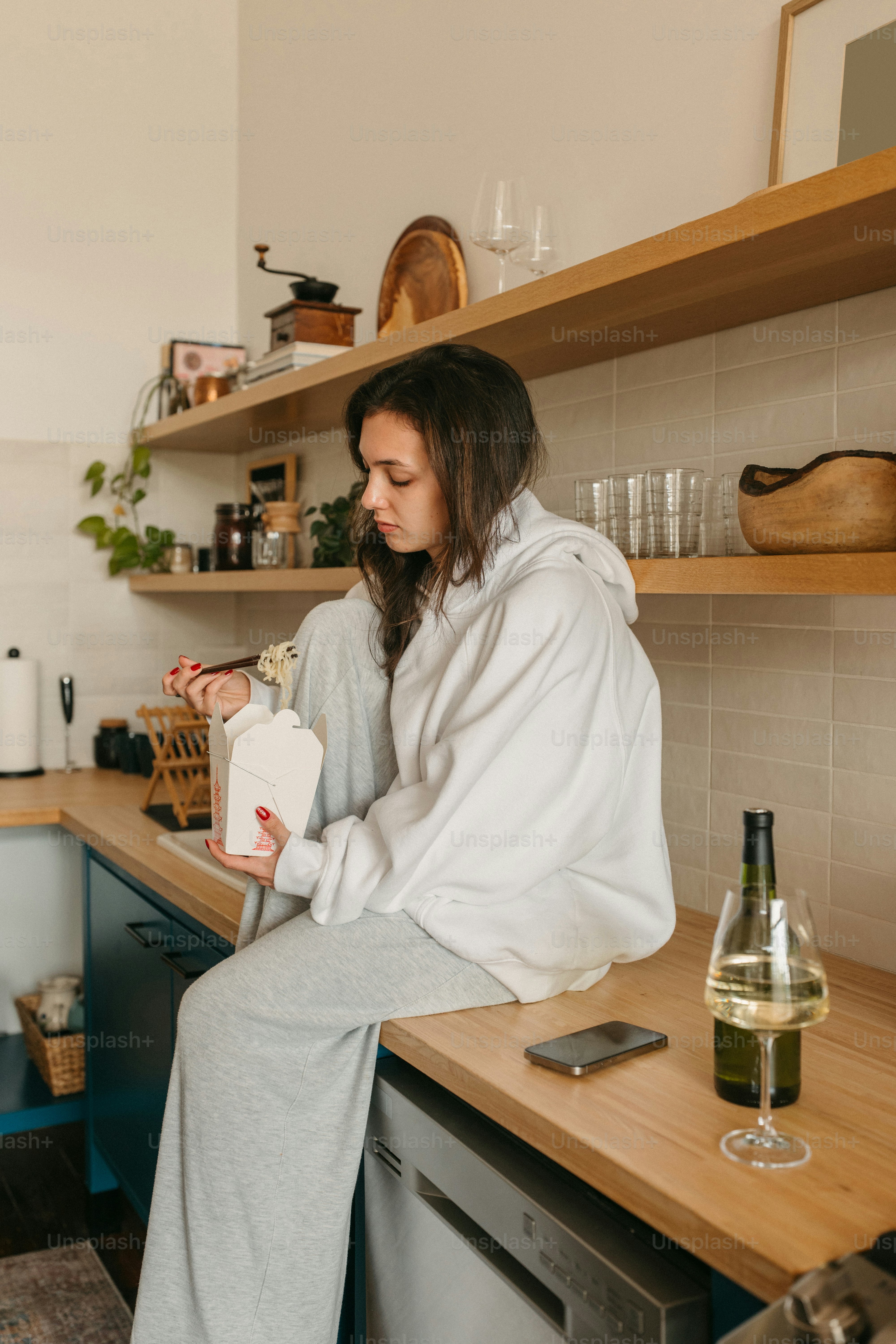 Woman in hoodie enjoys takeout in her kitchen.