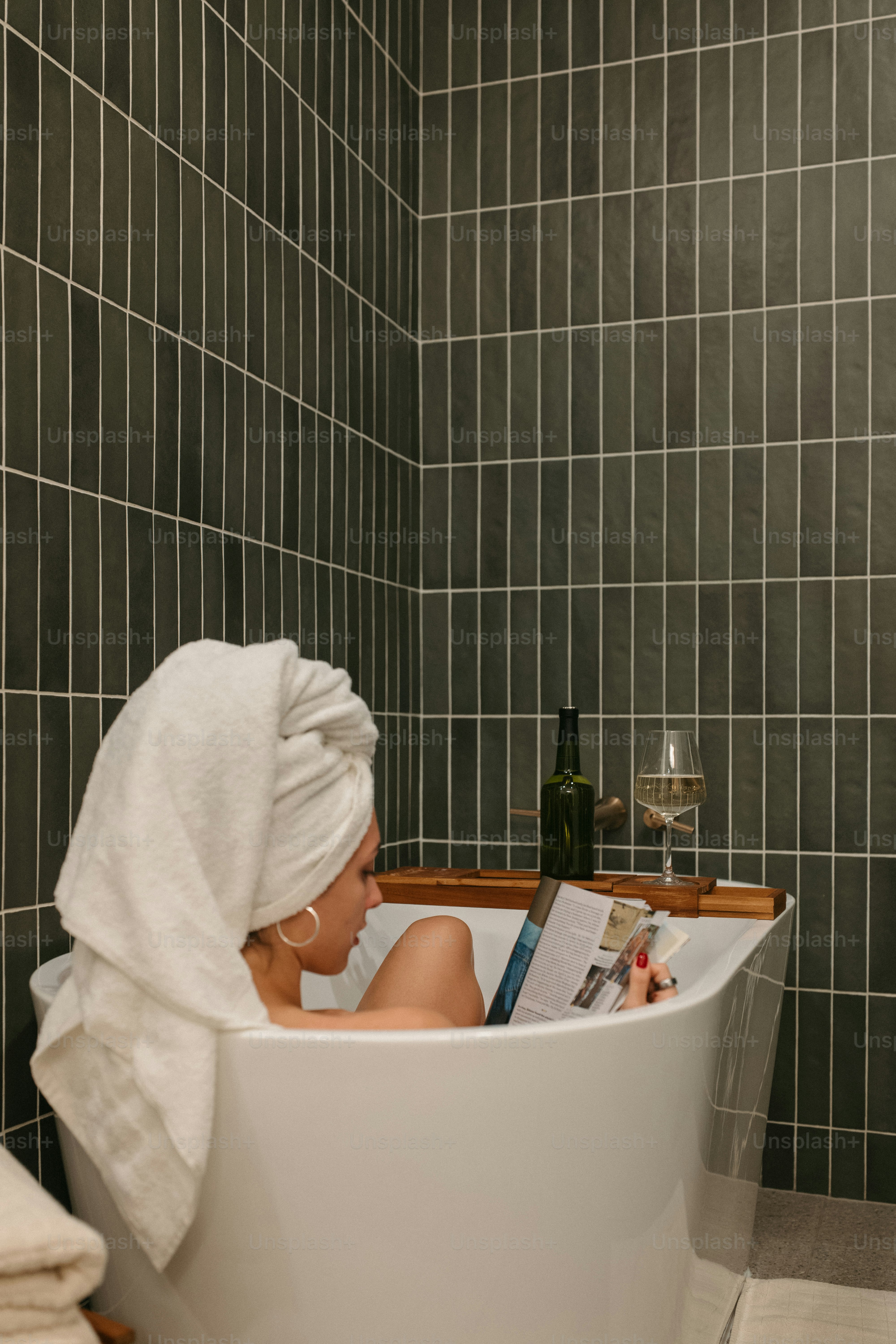 Woman relaxing in a bathtub with a drink and reading.