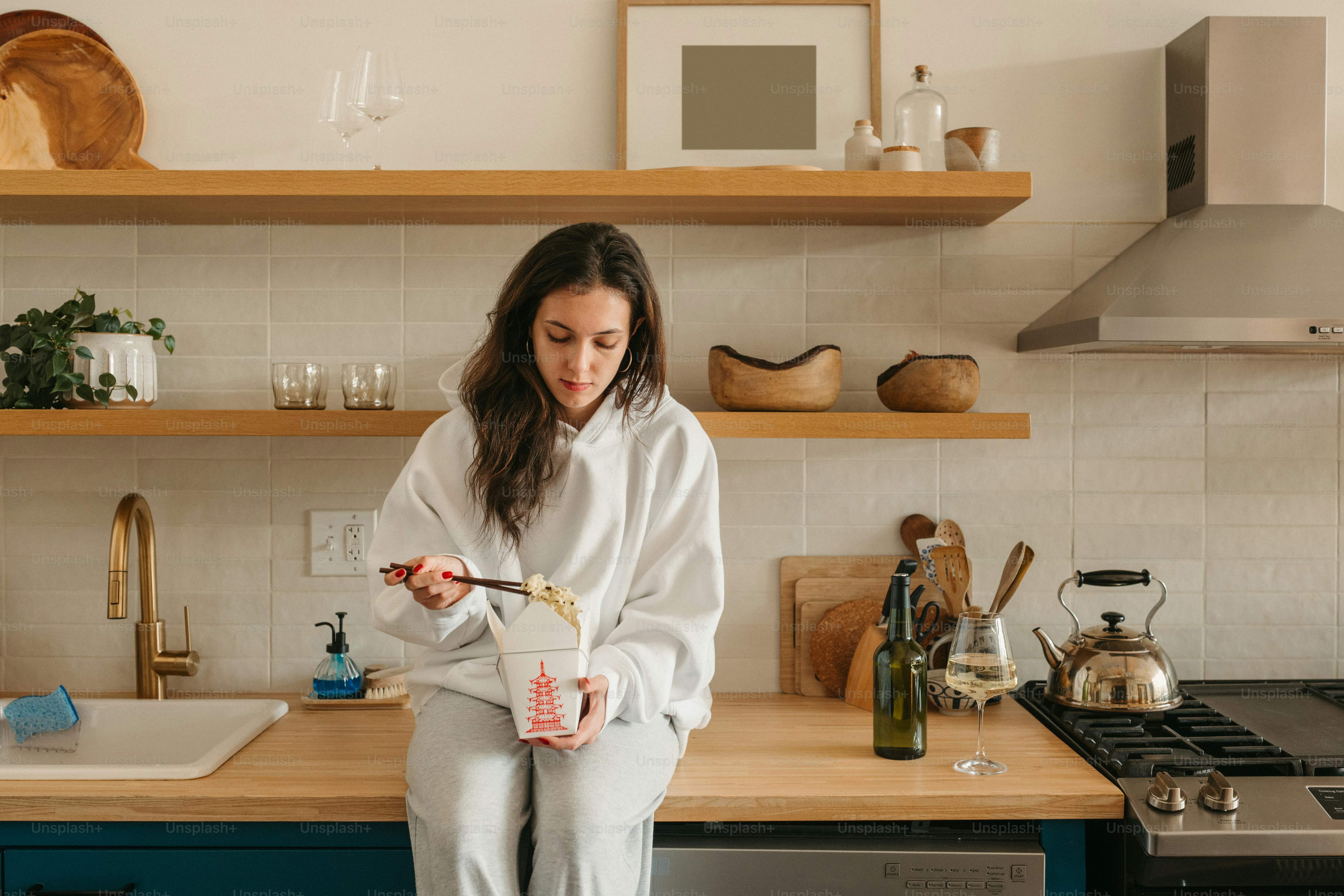 Woman enjoys takeout noodles in a cozy kitchen.