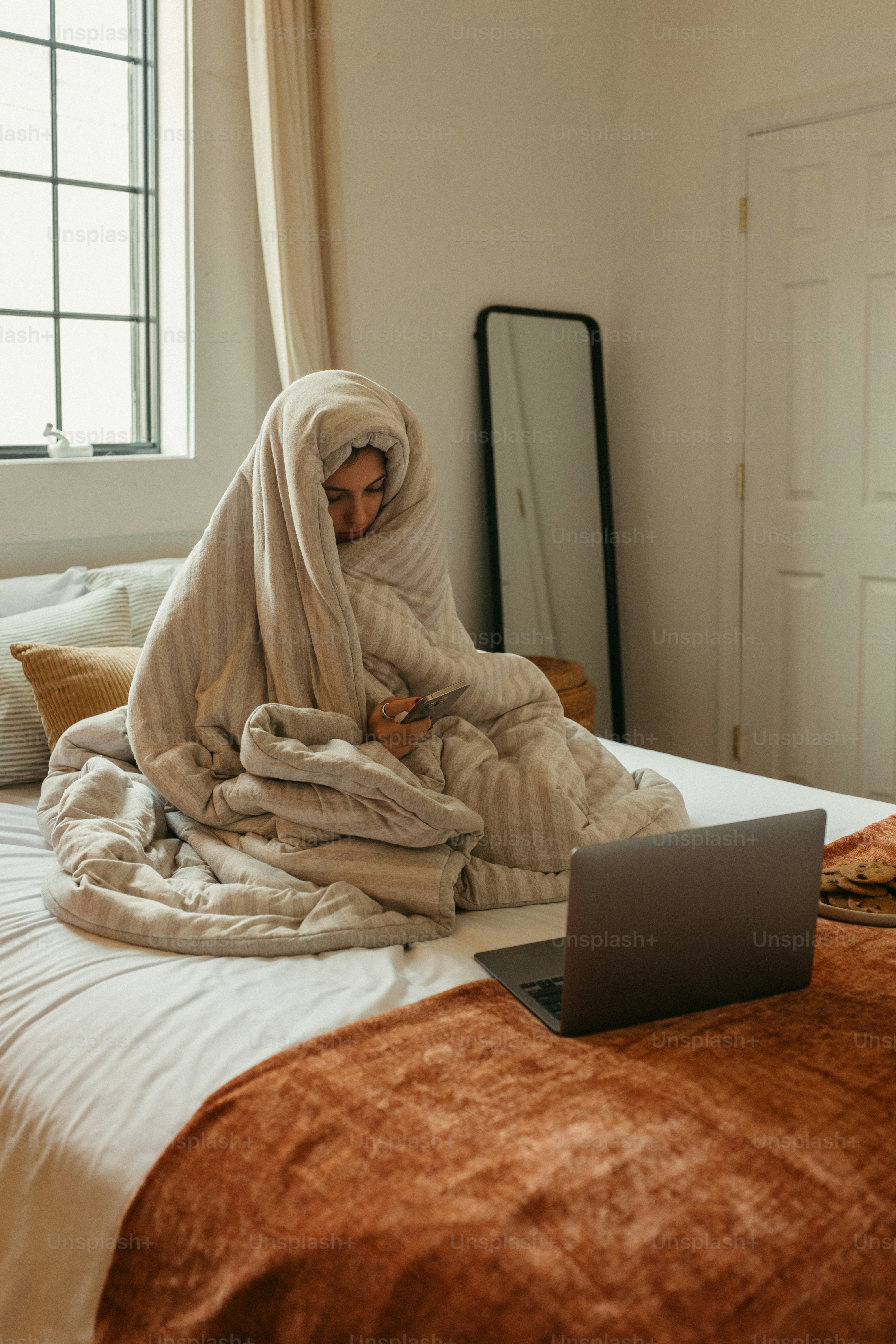 Woman wrapped in blanket uses a laptop.