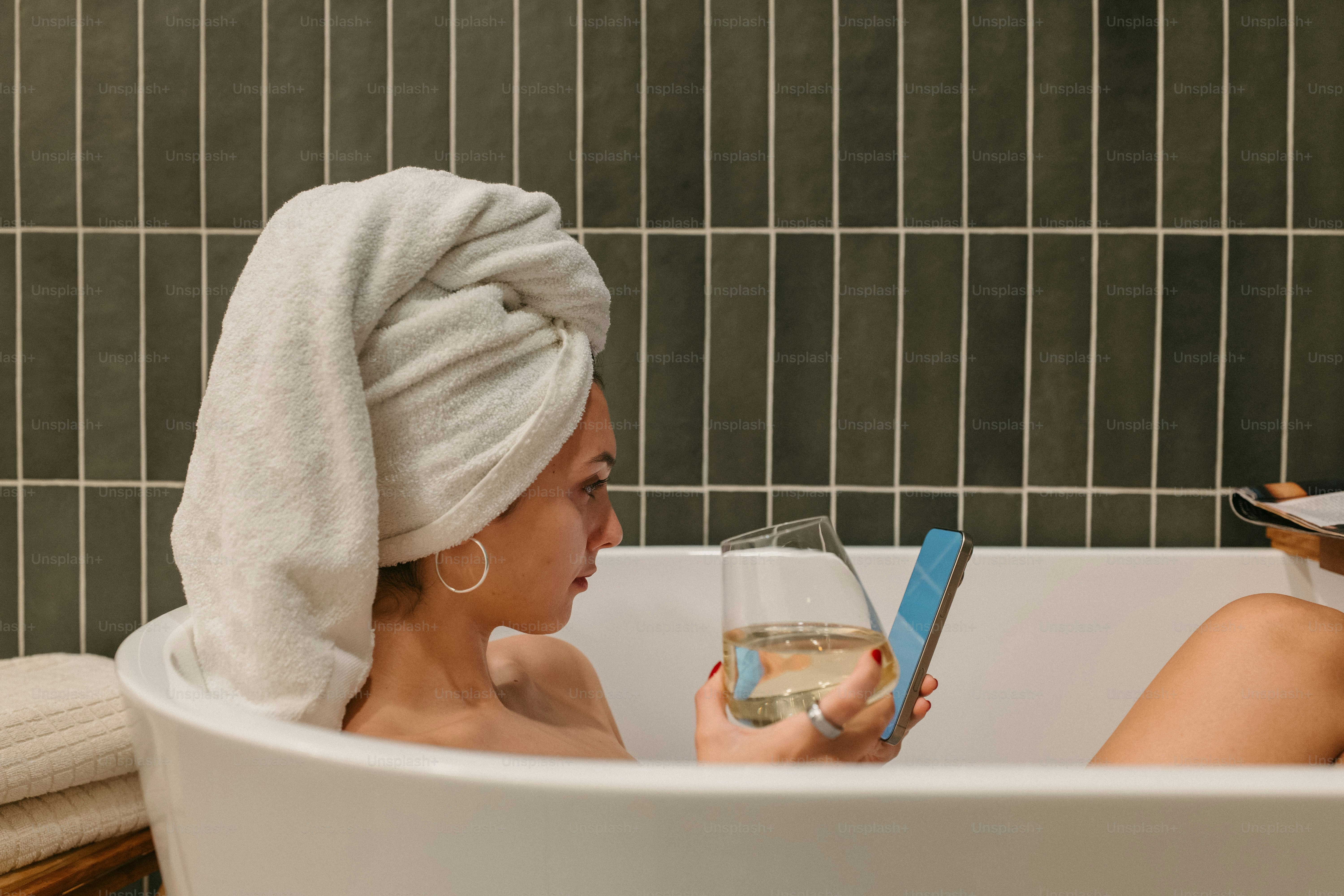 Woman enjoys a bath with a drink and her phone.