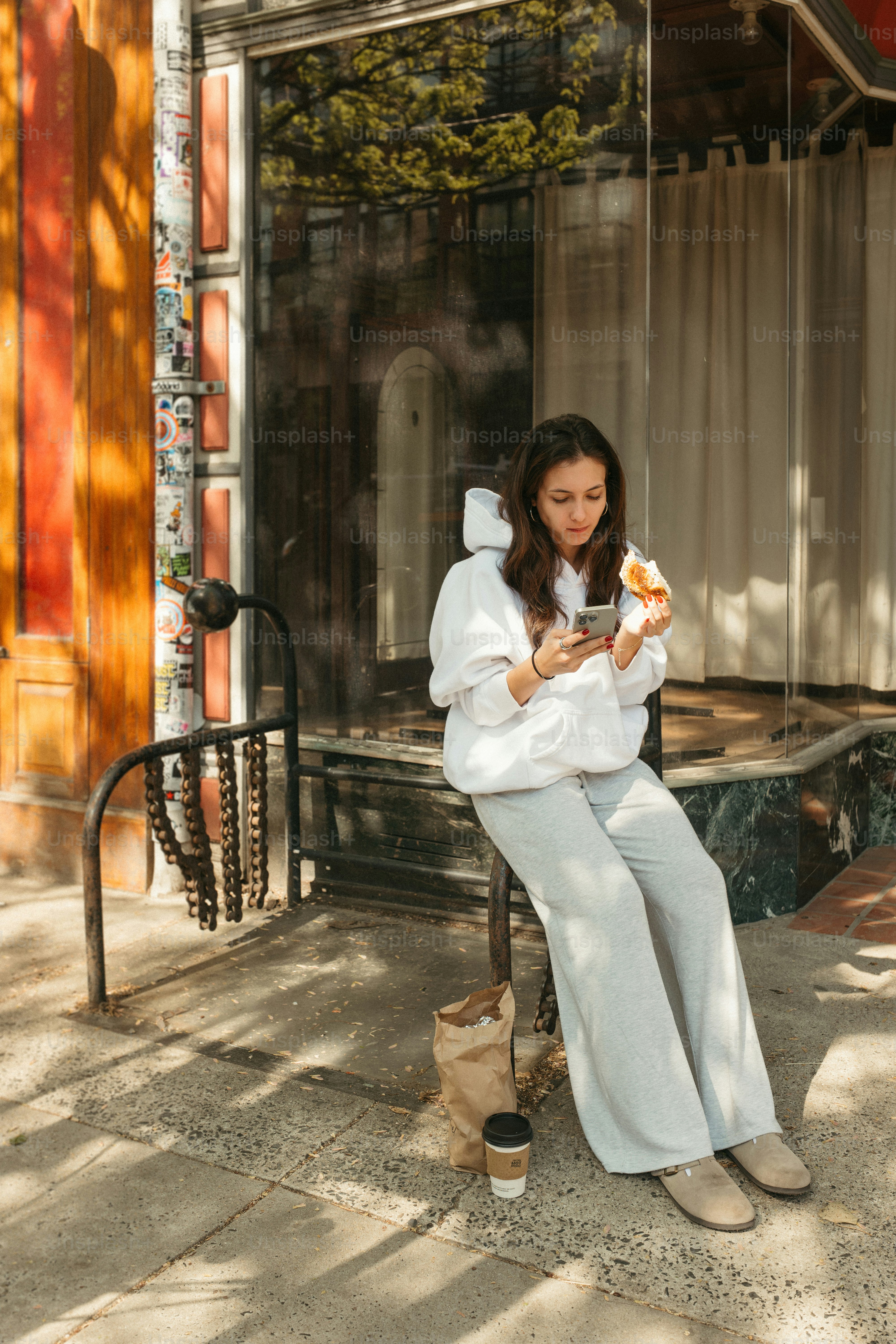 A woman eats pizza while looking at her phone.