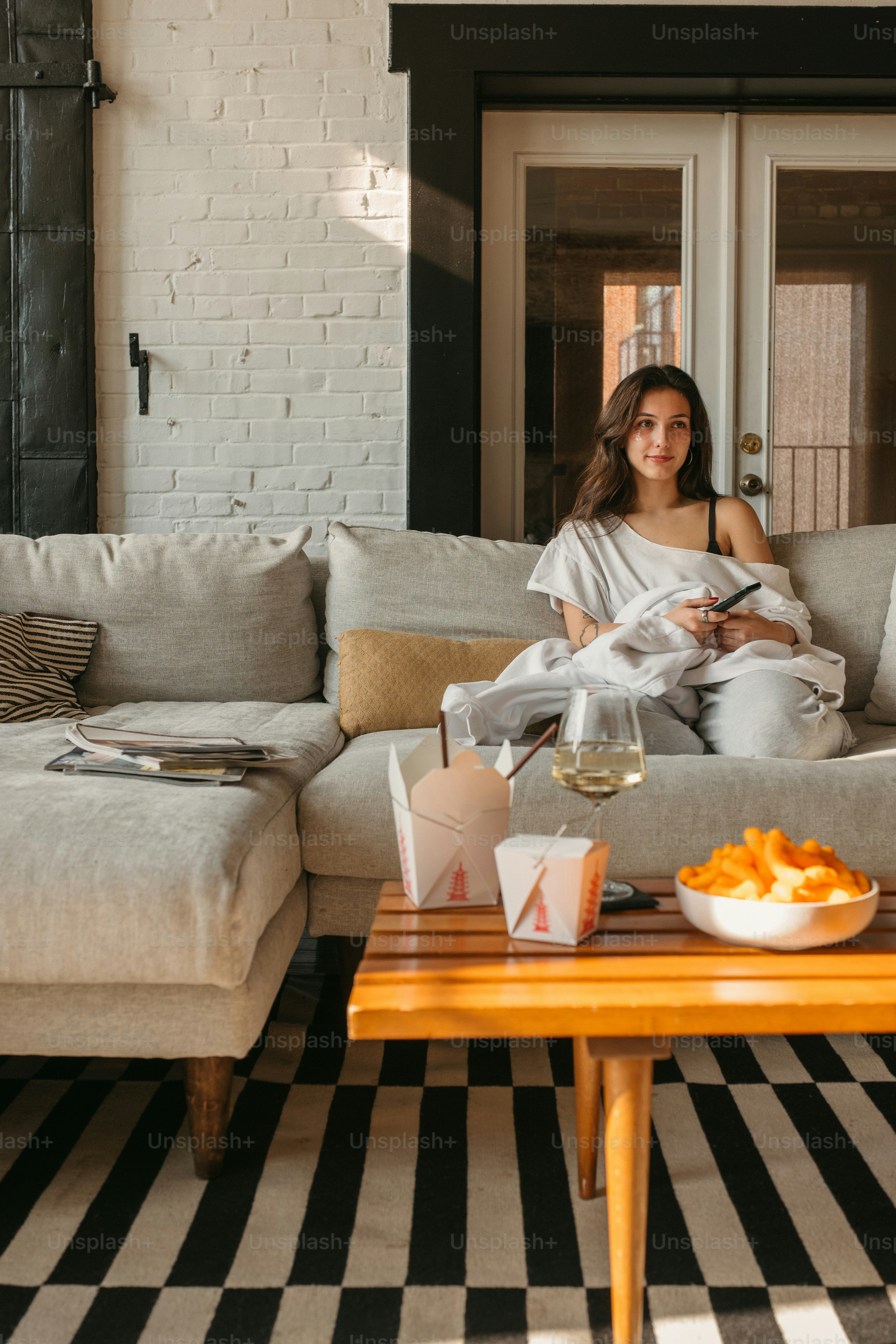 Woman relaxes on couch with snacks and drinks.