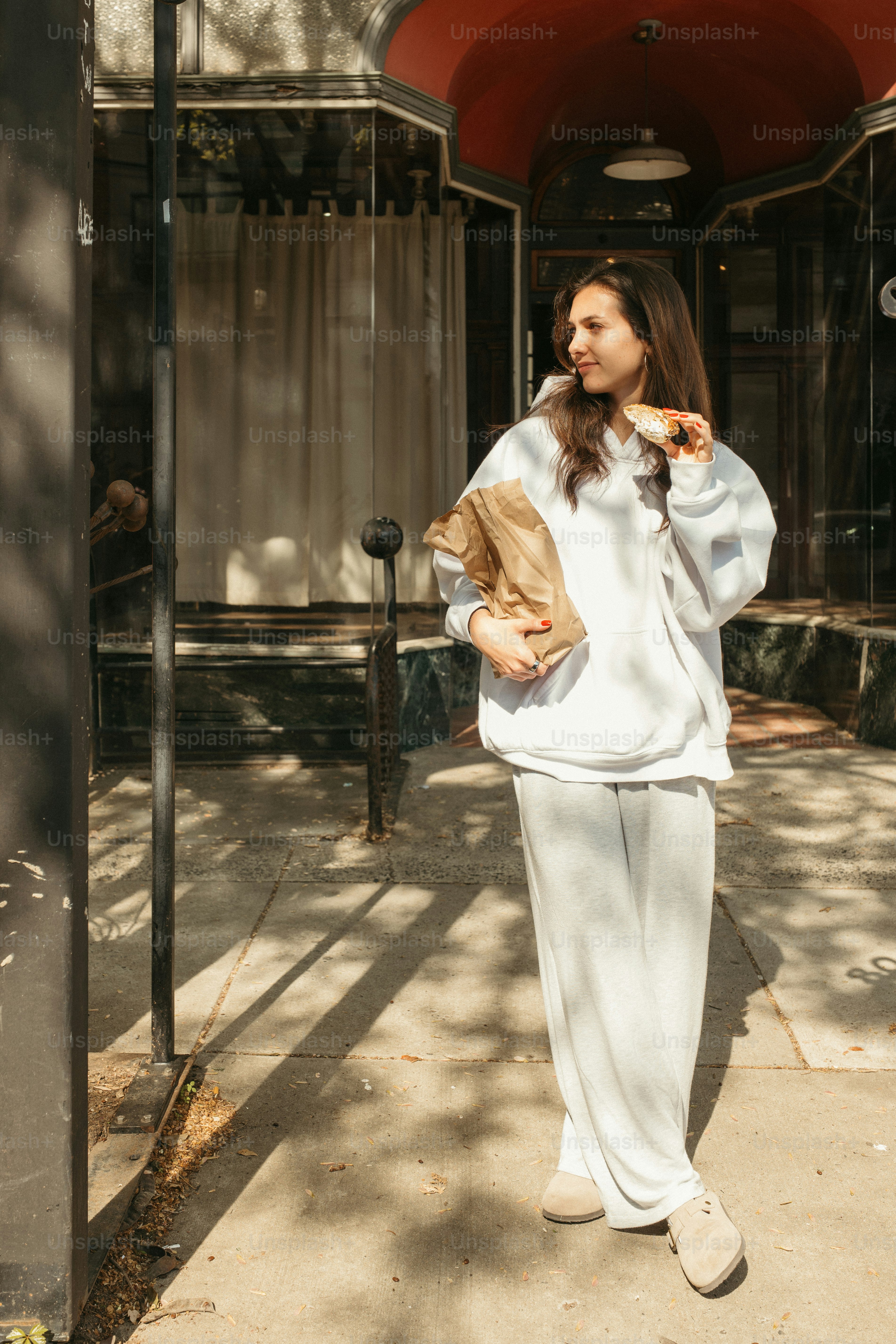 A woman stands holding a bag outside.