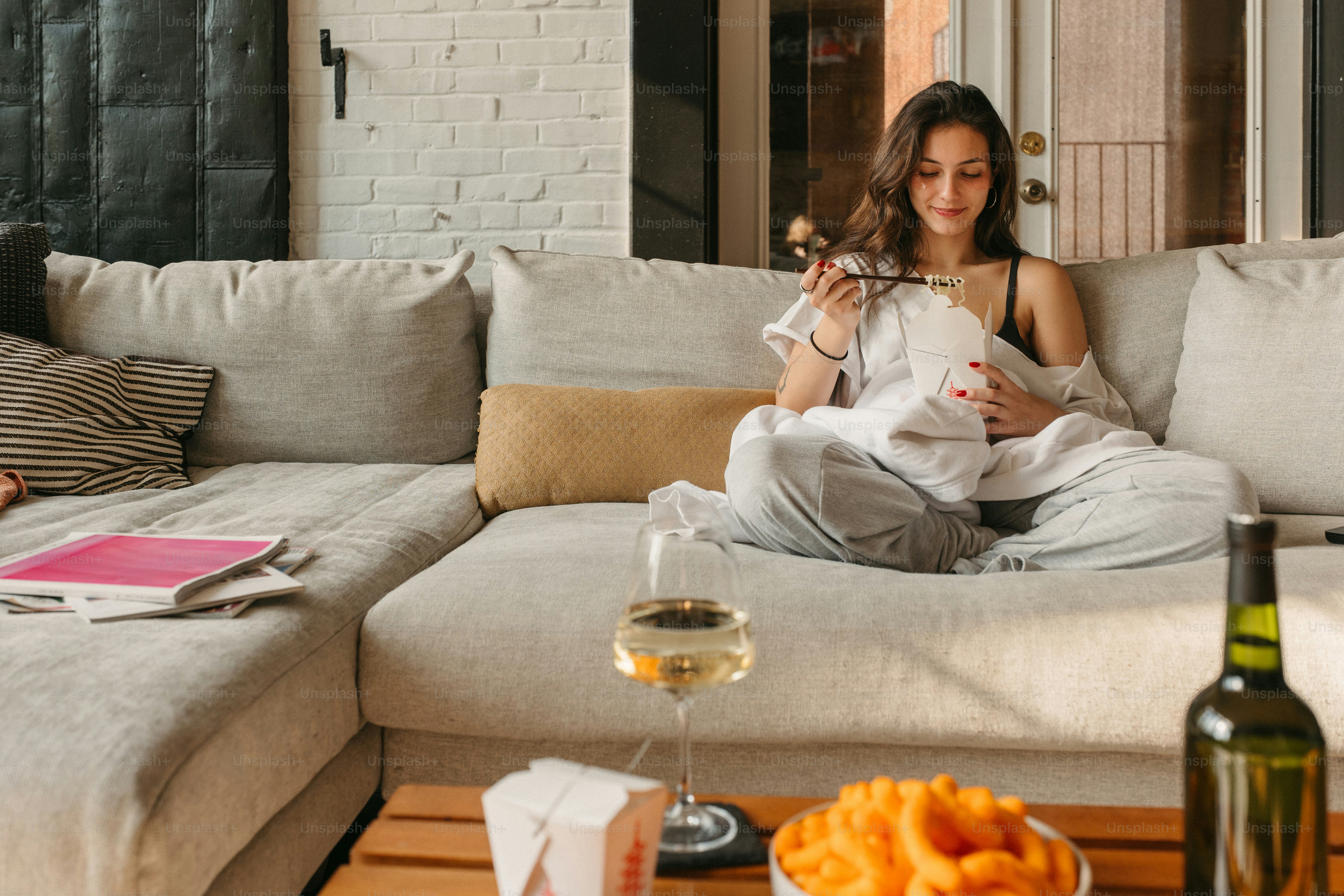 Woman relaxes on a couch with food and wine.