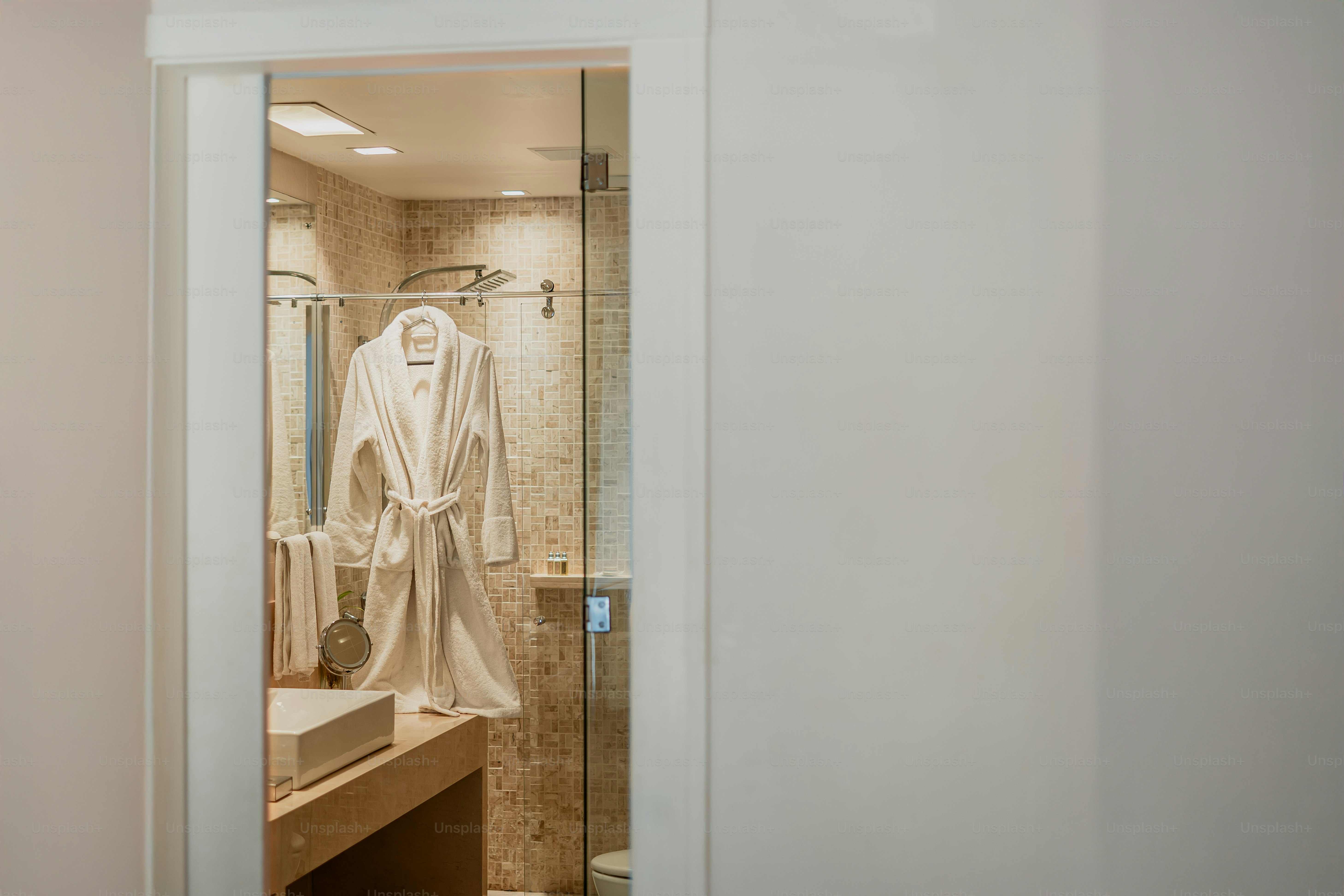 A bathrobe hangs in a glass-walled shower.