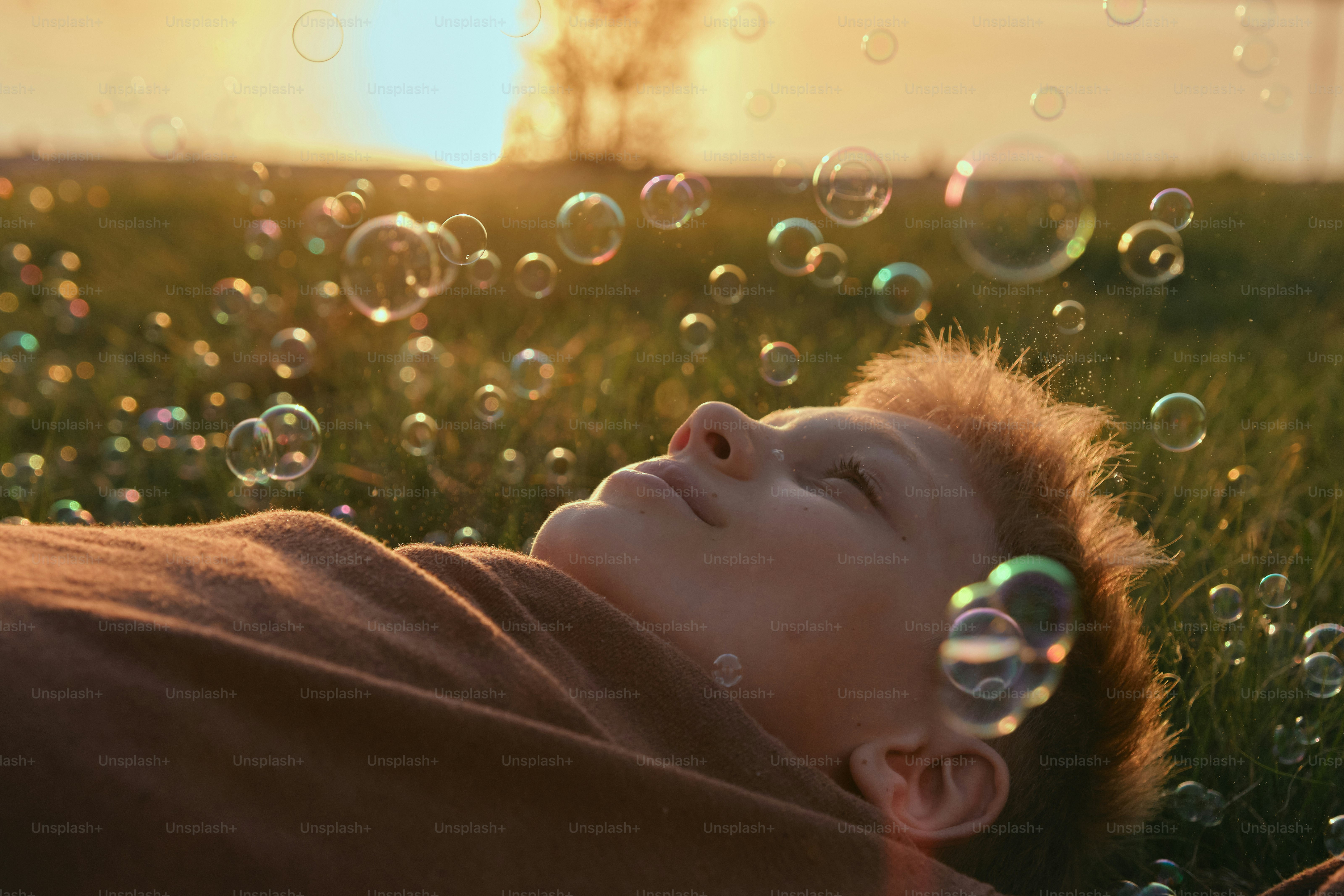 Boy relaxes in grass while watching bubbles.