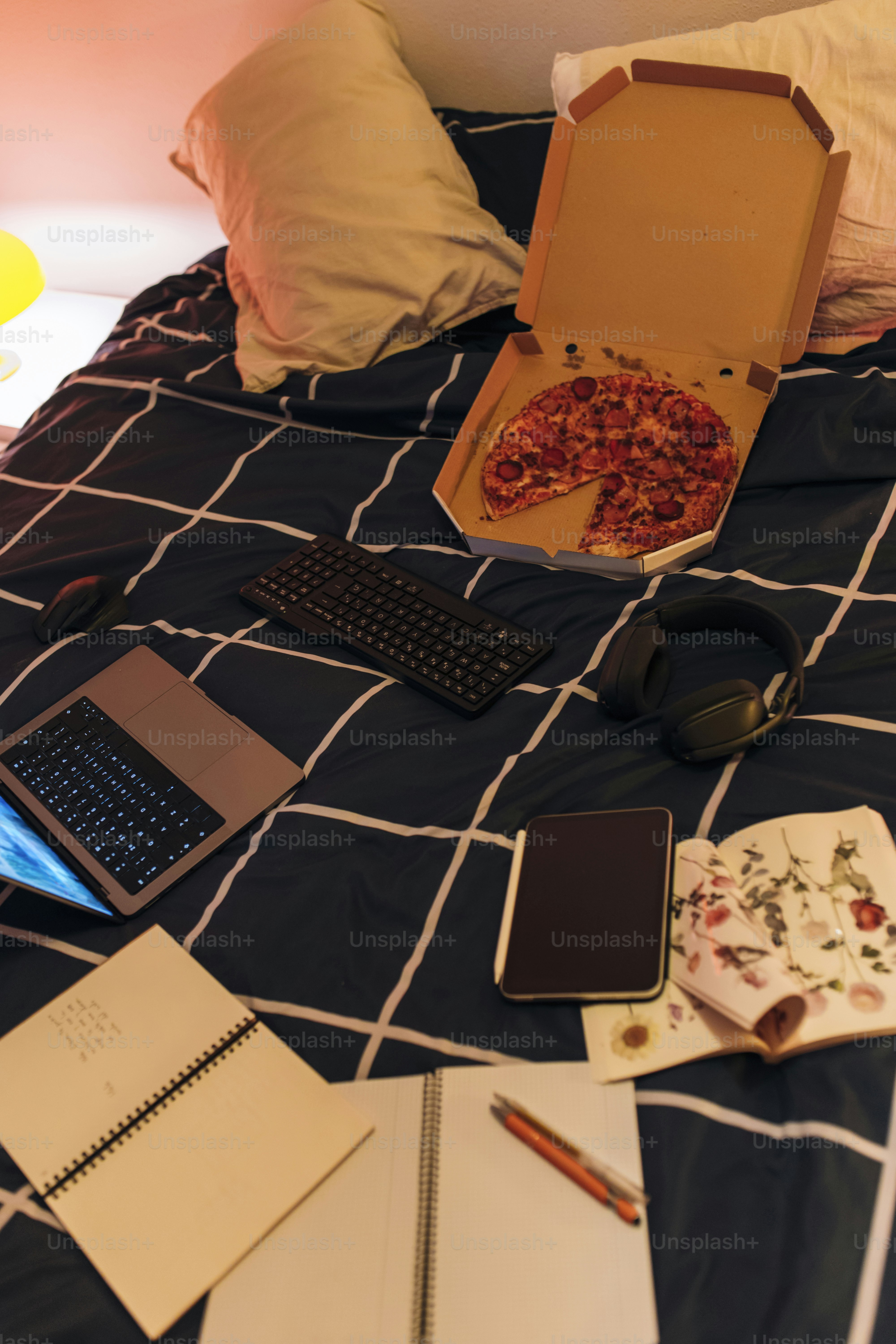 Pizza and tech sprawl across a messy bed.
