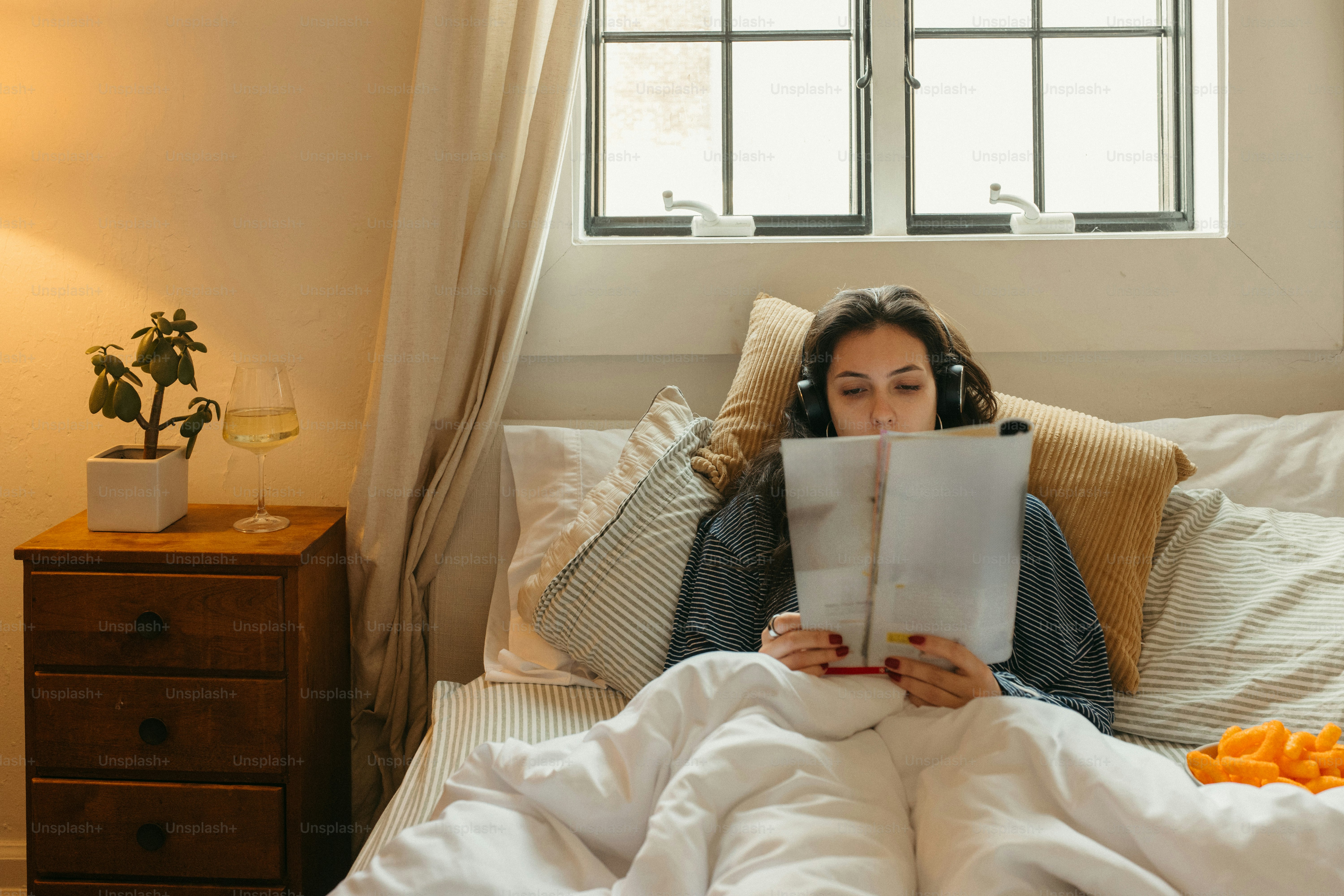 Woman reads in bed with headphones on.