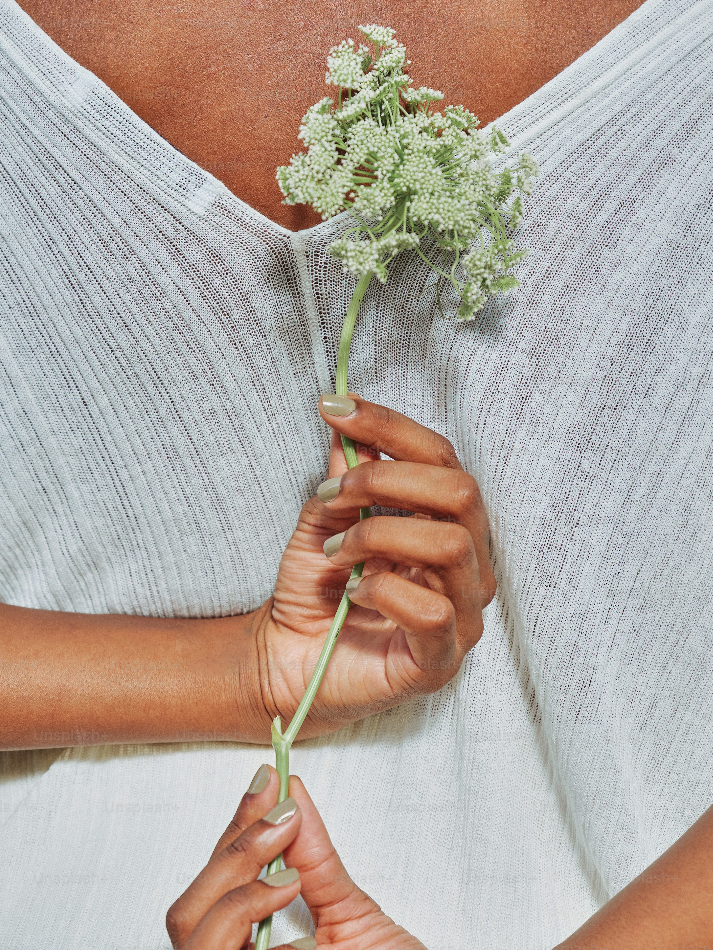 Woman holds a delicate flower against her chest.