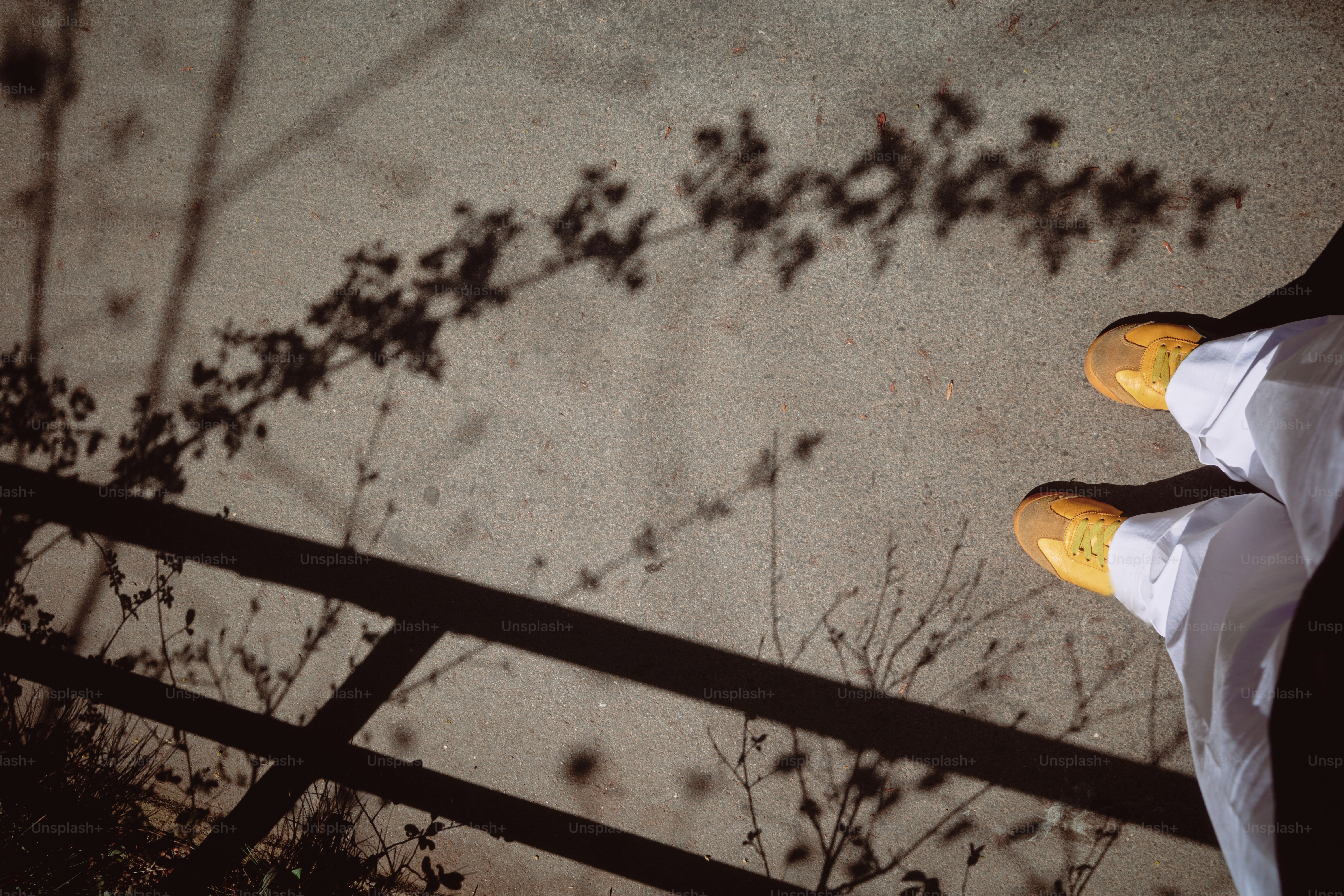 Schatten fallen auf eine Betonfläche mit gelben Schuhen.