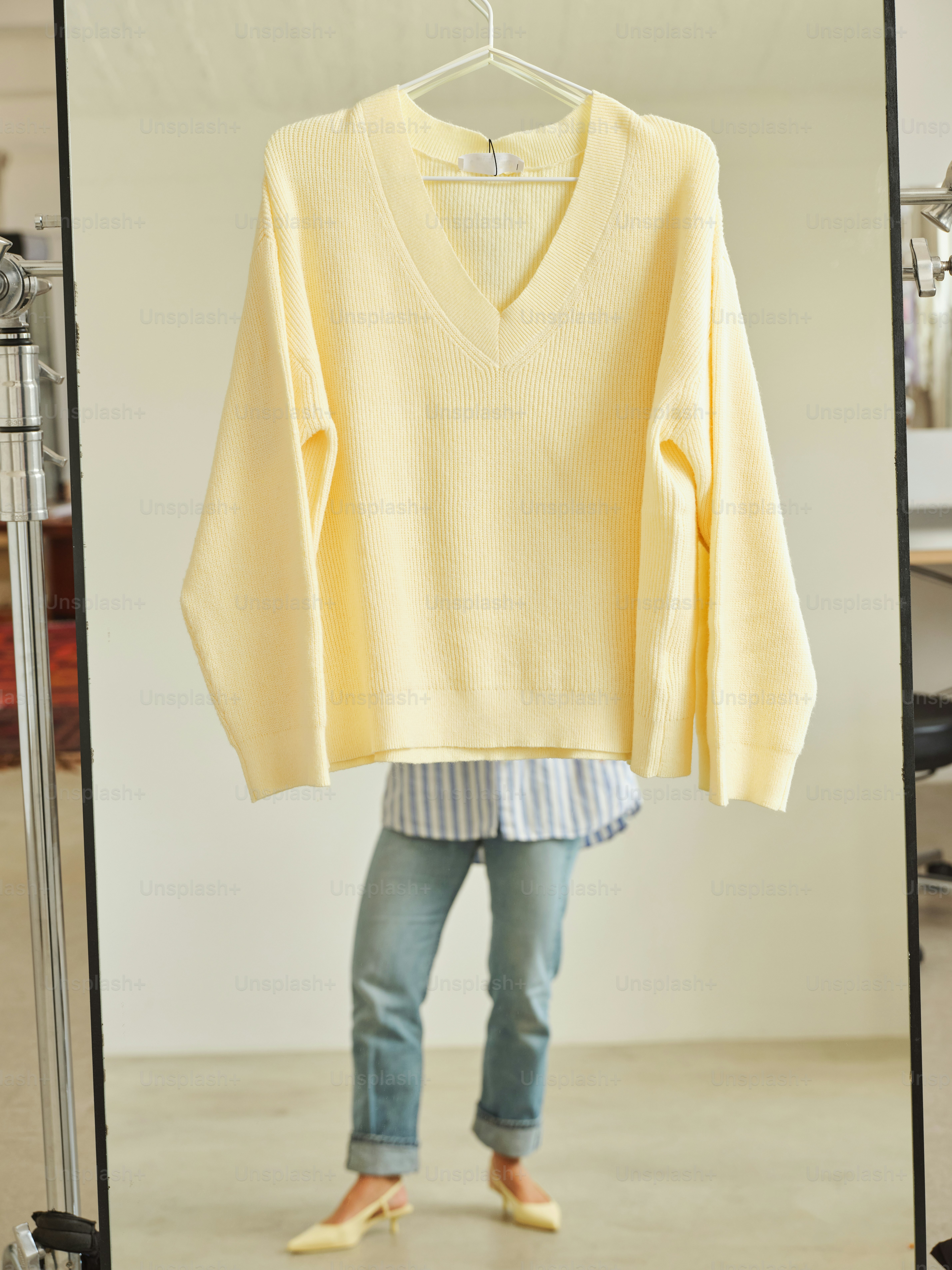 Seseorang memodelkan sweter kuning dan jeans.