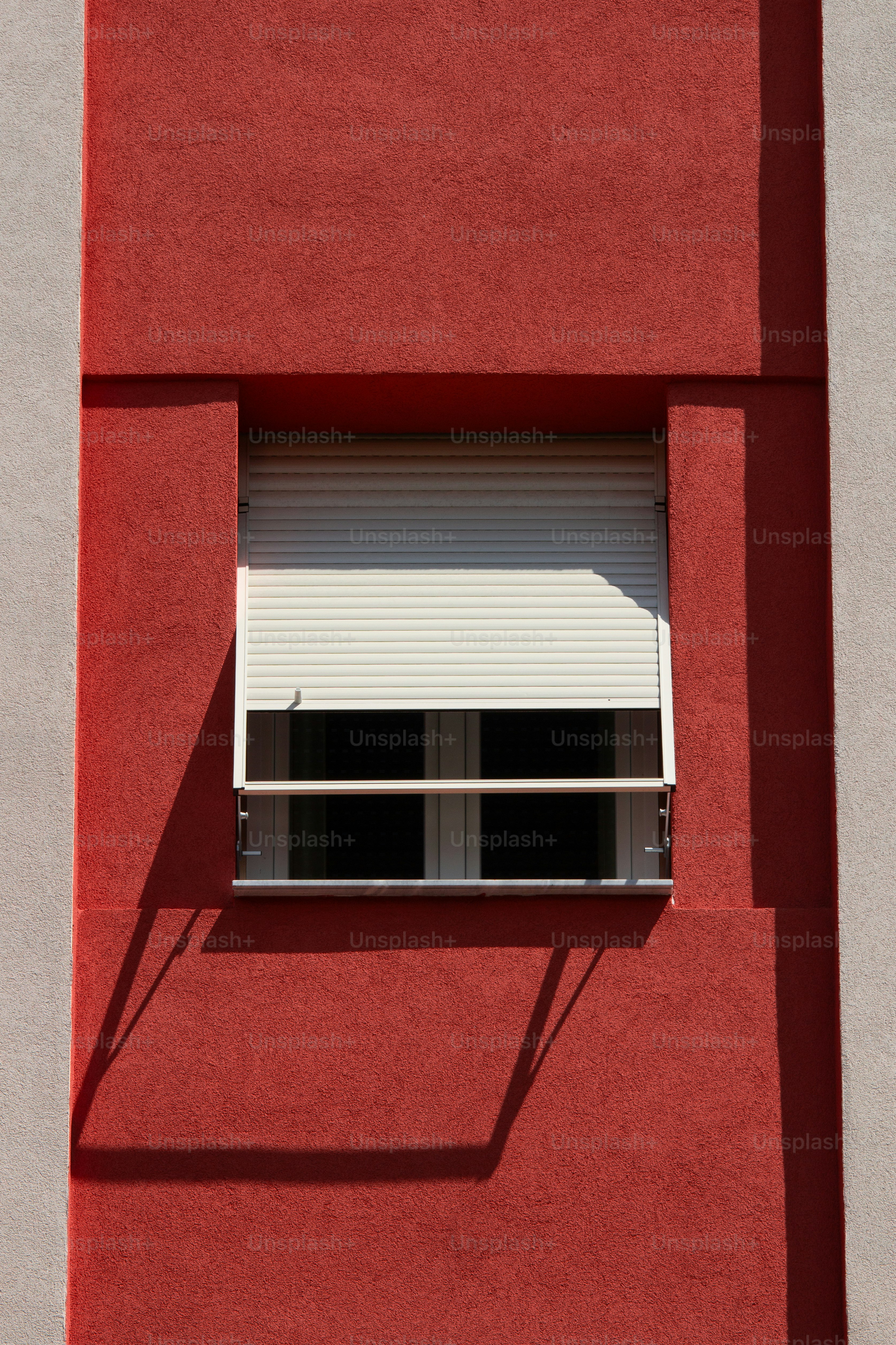 Window with closed blinds on a red wall.